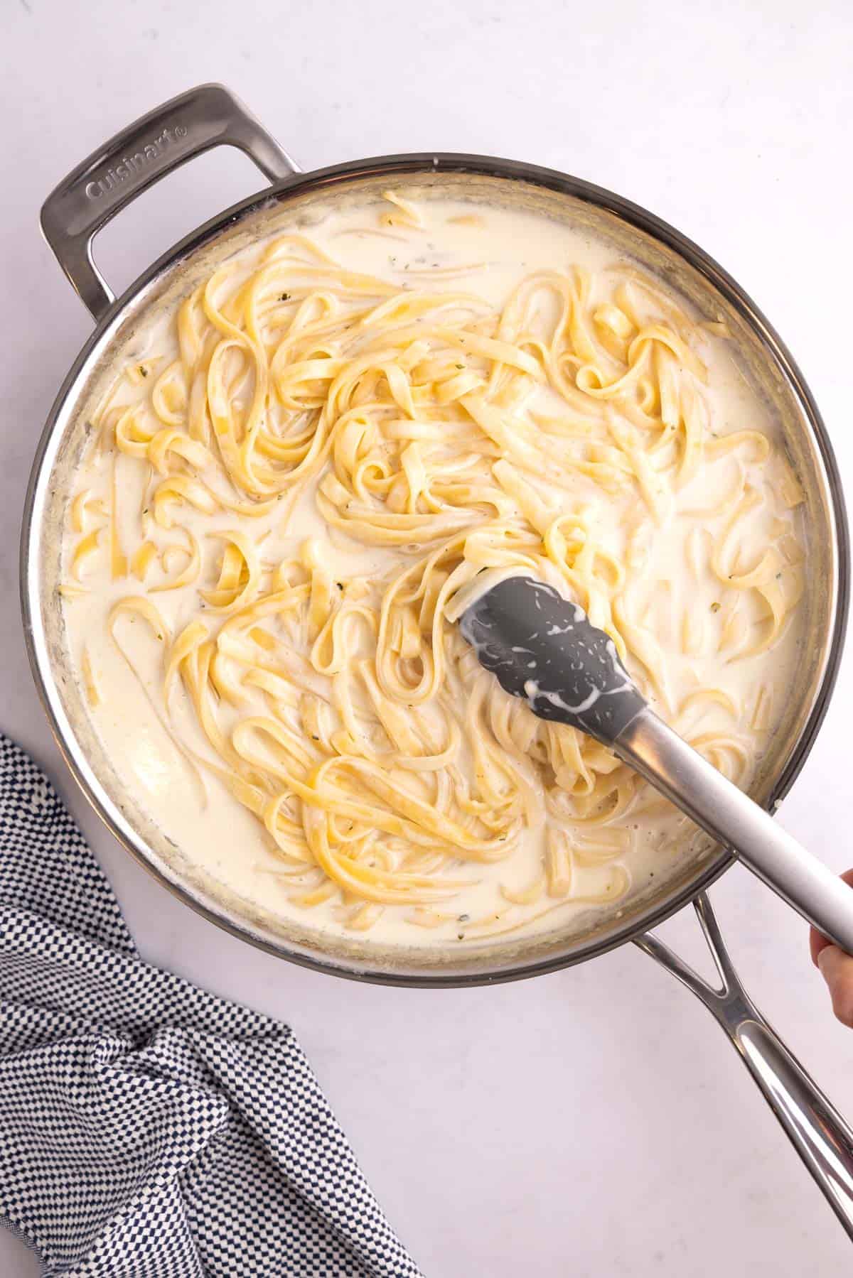 Stirring a pot of alfredo with tongs.