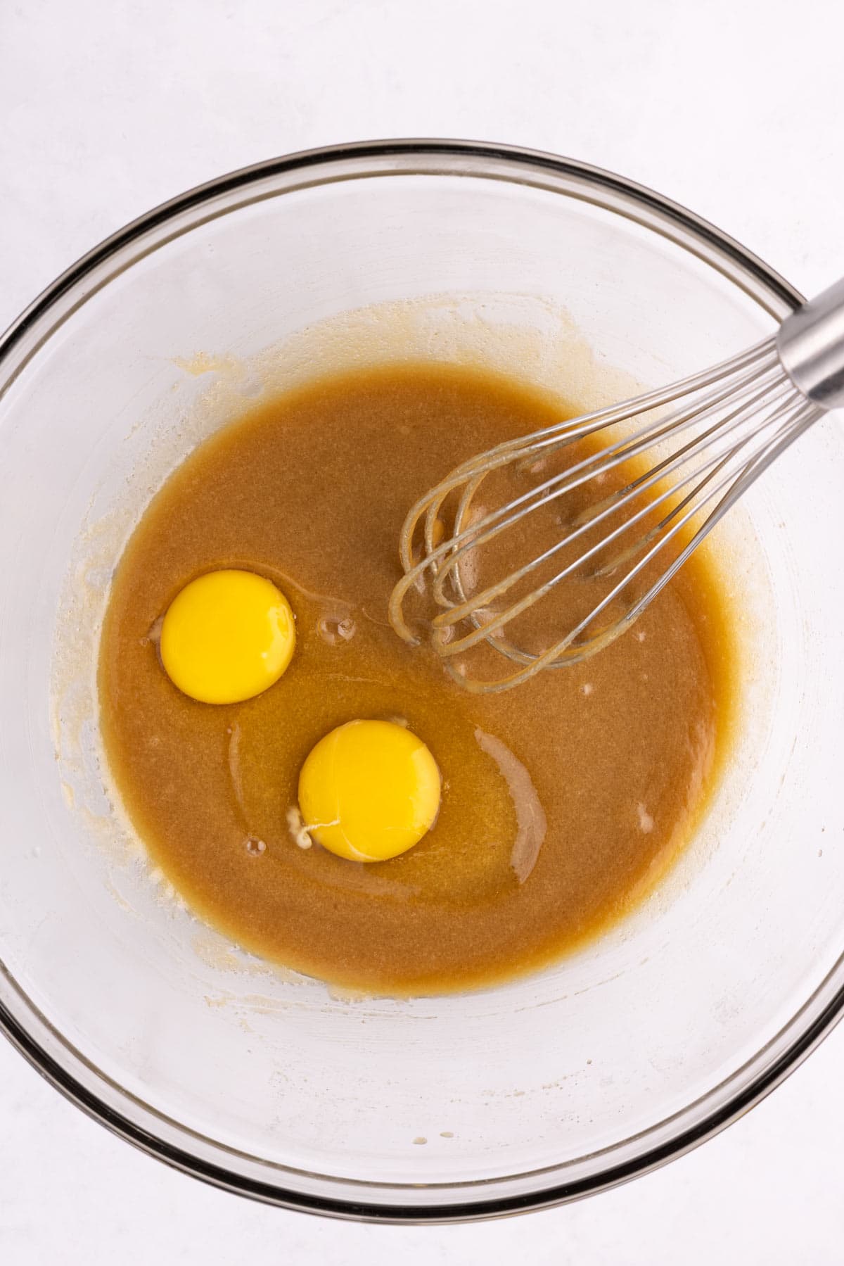 Eggs added to a bowl of batter with a whisk.
