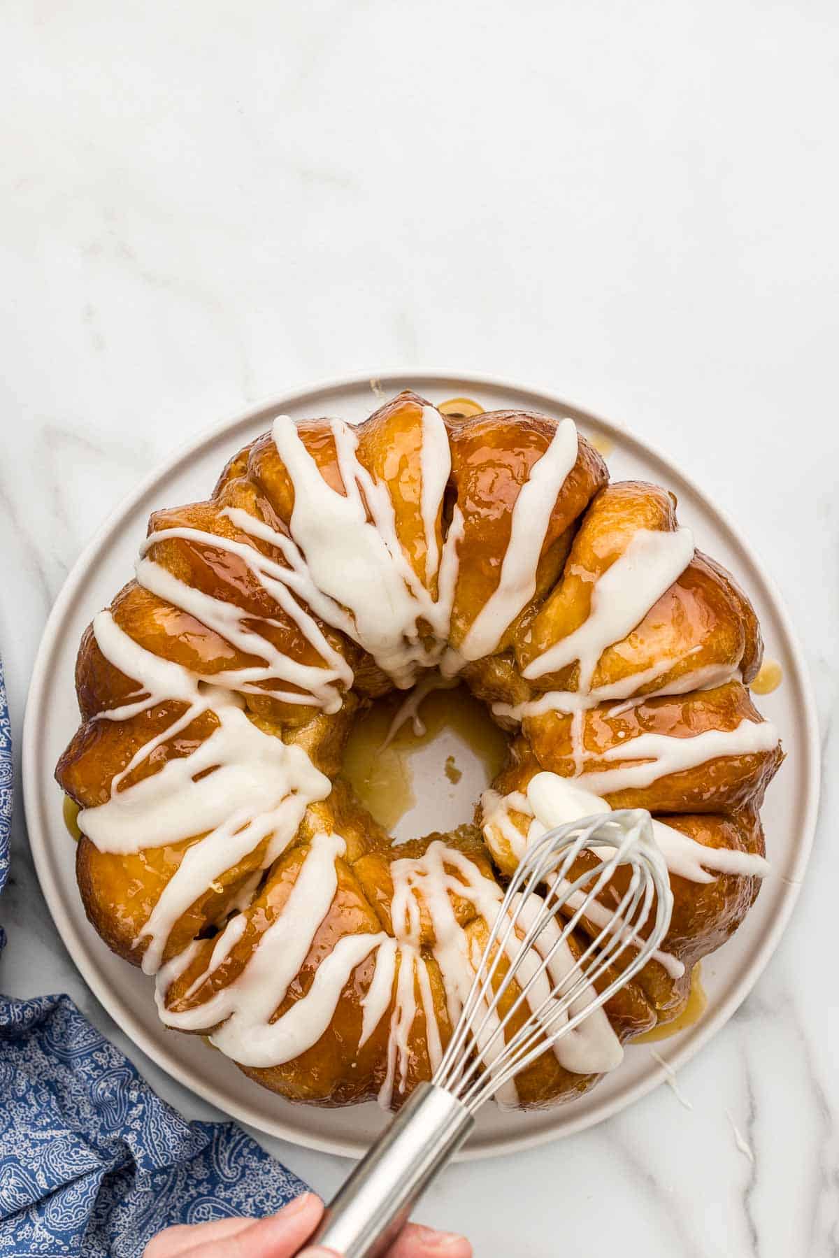A whisk drizzling frosting over lemon monkey bread on a platter.