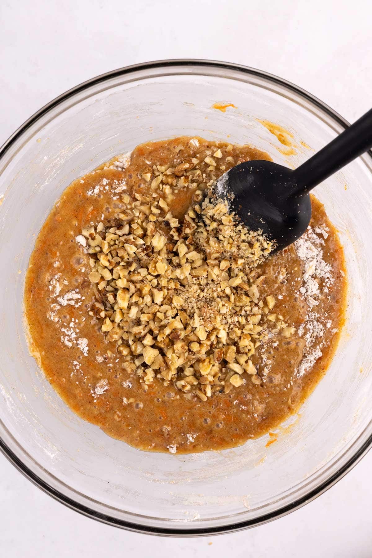 Chopped nuts added to a mixing dish with a spatula.