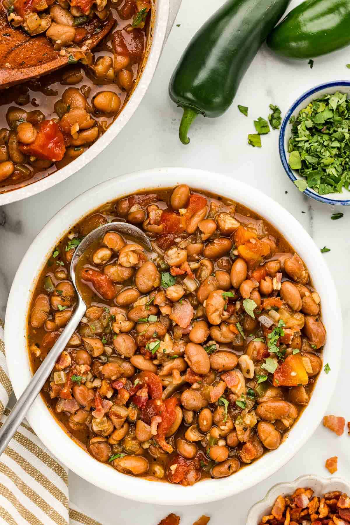 A serving of borracho beans in a white bowl with a spoon.