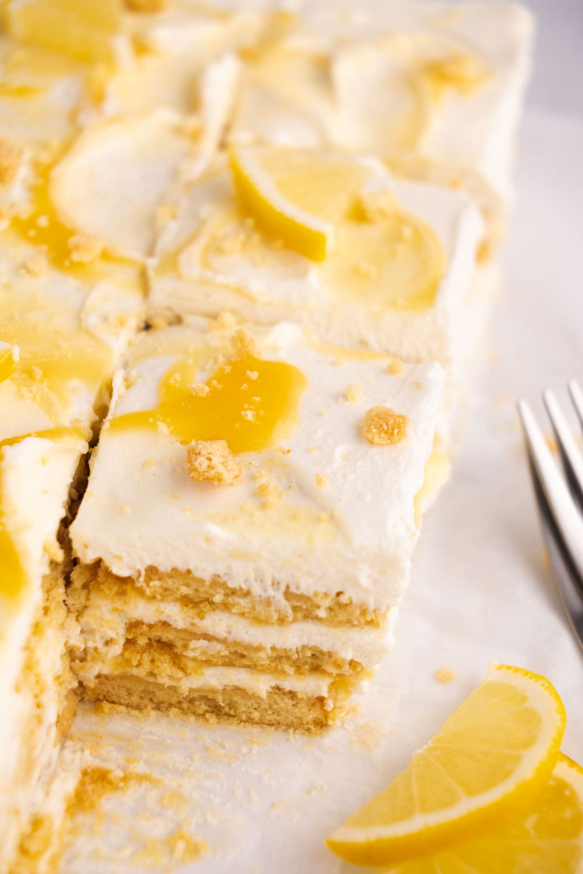 Lemon icebox cake squares on parchment with lemon slices beside them.