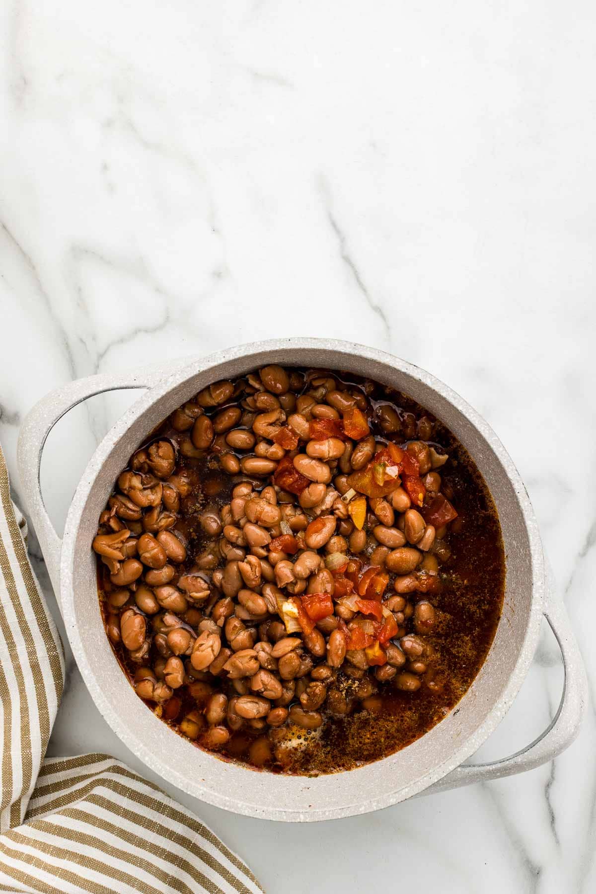 Borracho beans sitting in juices in a white cooking pot.