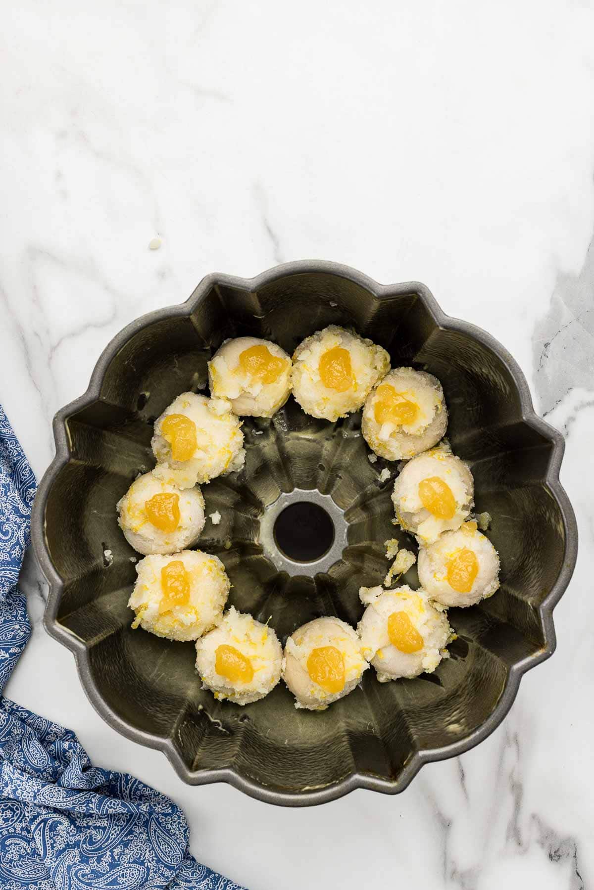 One row of dough balls and lemon filling at the bottom of a baking cake pan.