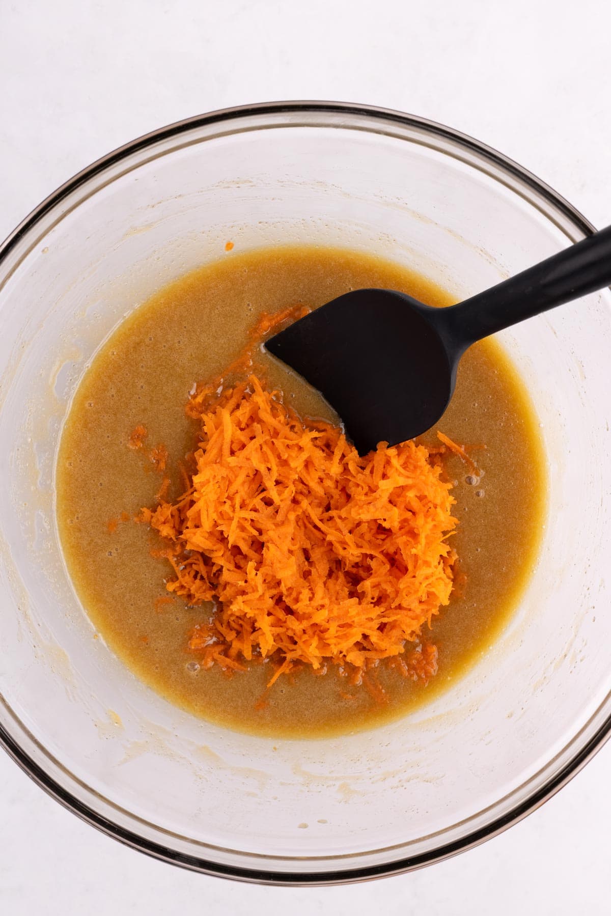 Carrots added to a bowl with a spatula.