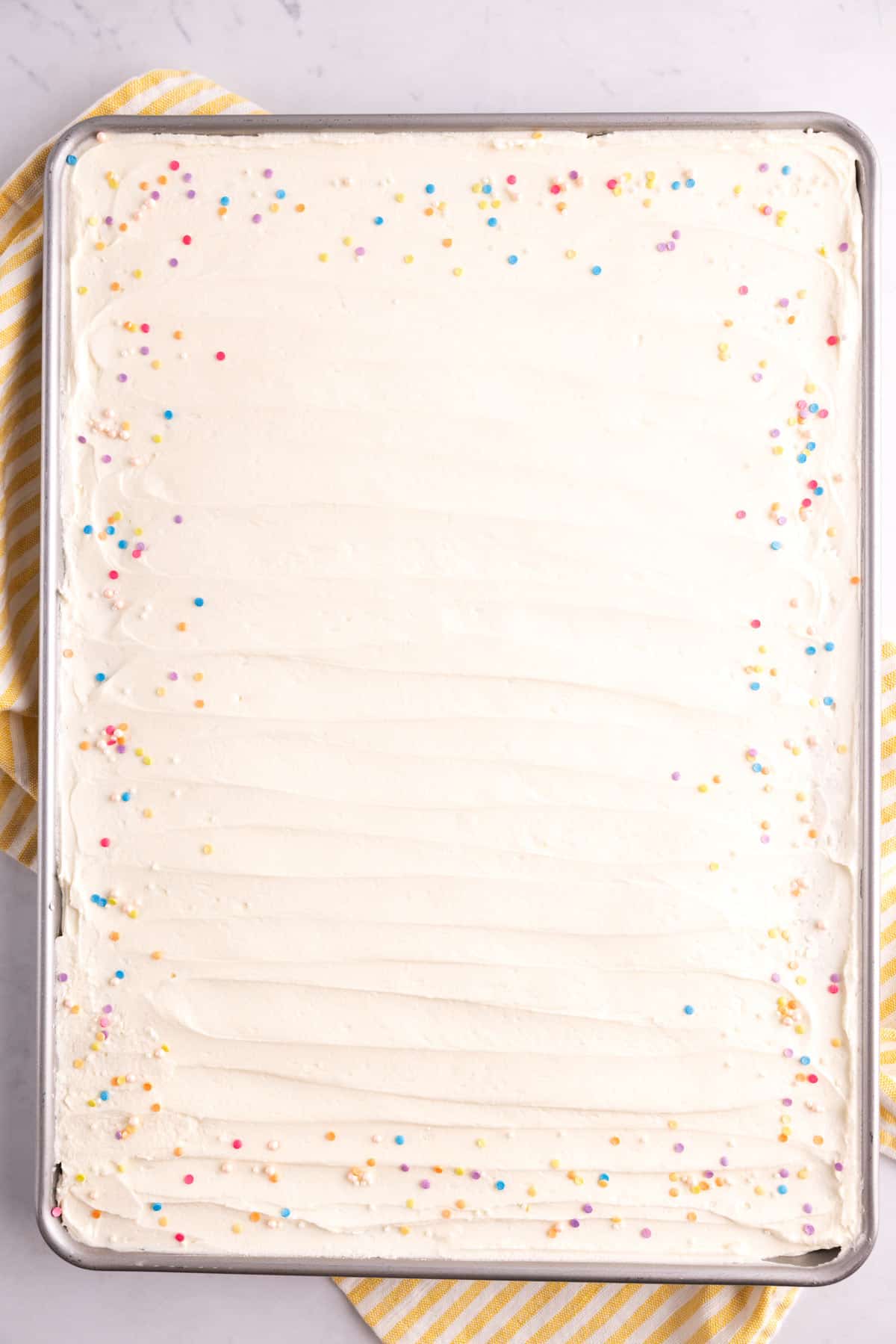 A pan of sugar cookie bars covered in white frosting with sprinkles.