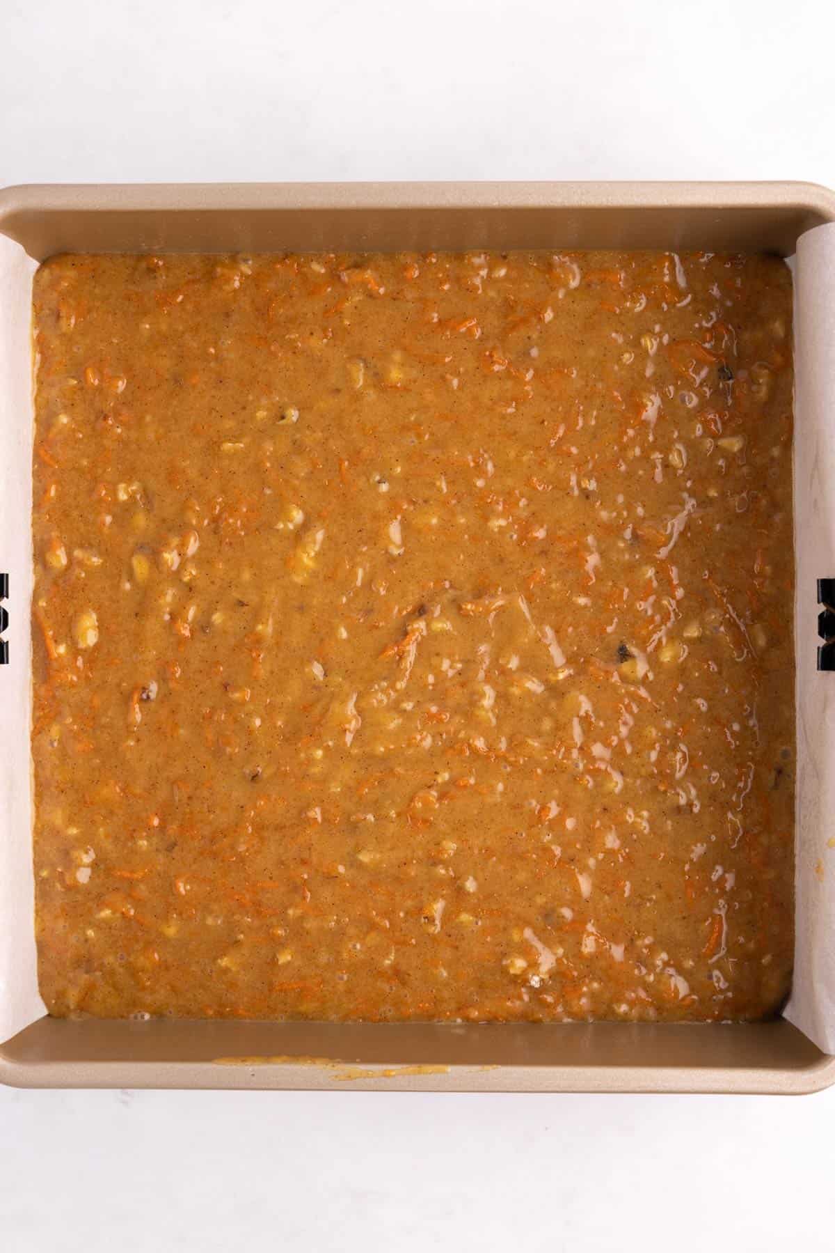 A square baking pan with carrot cake batter in it.