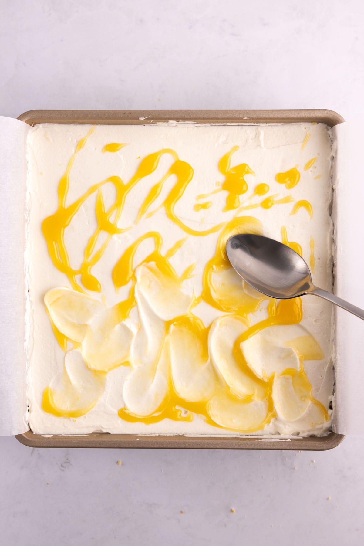 Lemon curd being rubbed over frosted cake in a baking pan with a spoon.