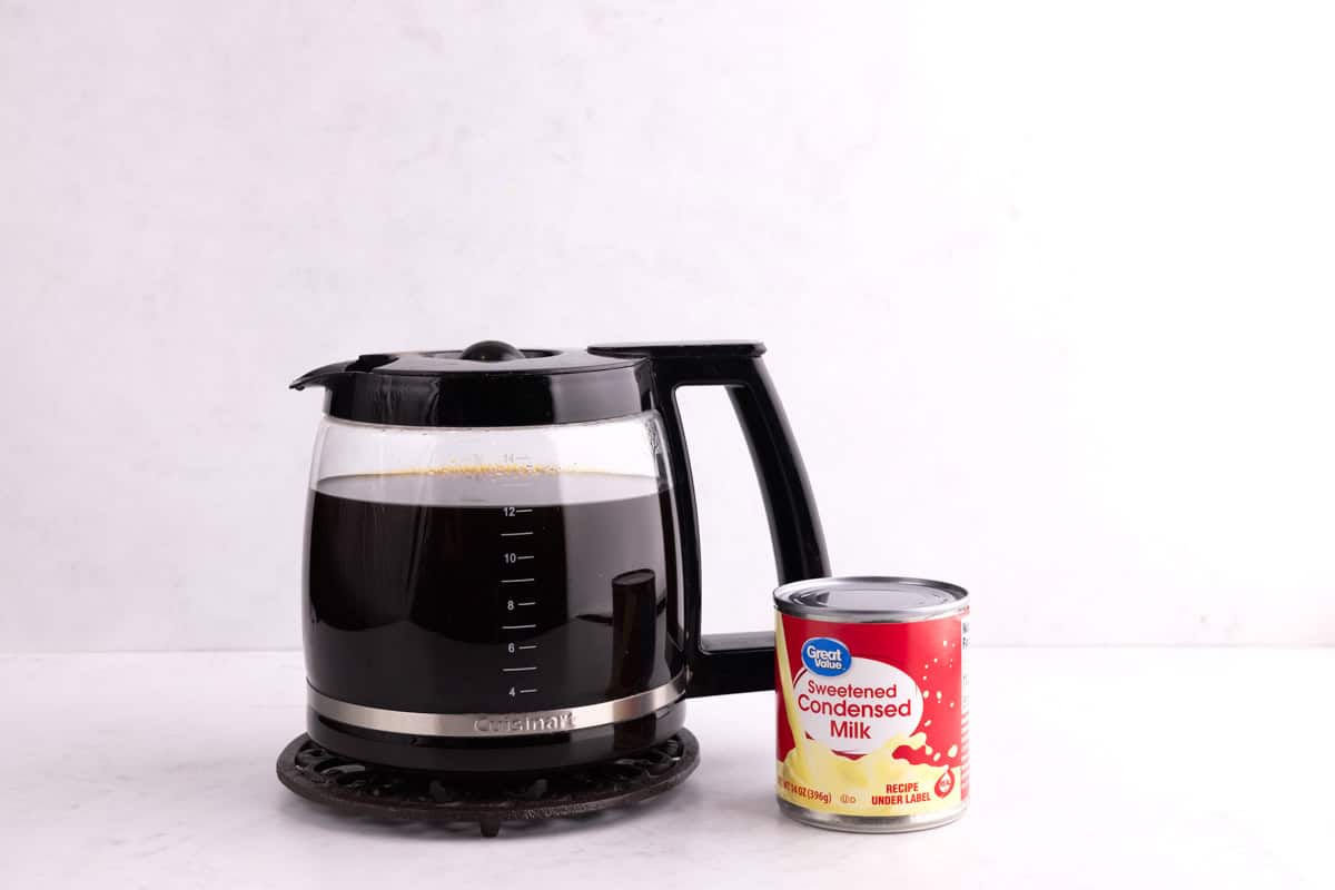 A pot of coffee and condensed milk on a white countertop.