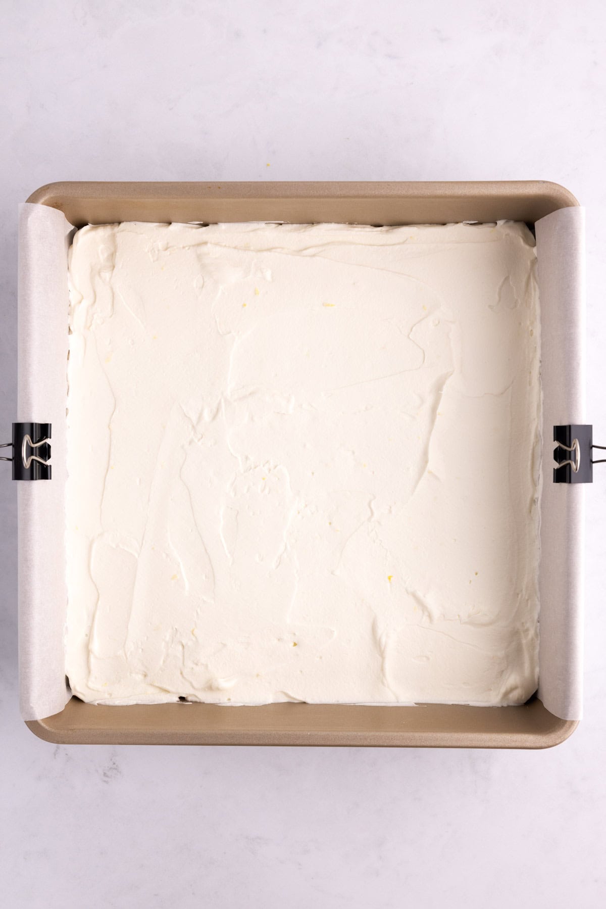 Whipped cream filling smoothed on top of shortbread cookies in a pan.