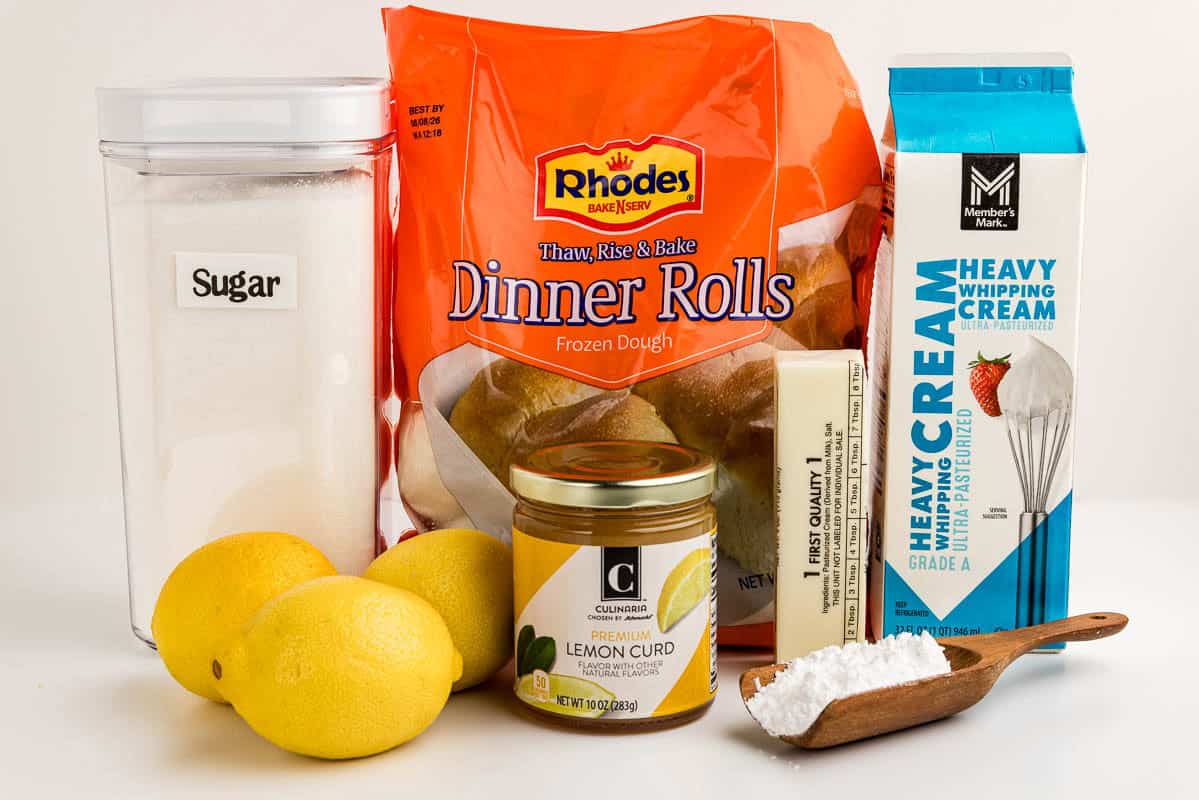 Sugar, lemons, lemon curd, frozen dinner rolls, butter, powdered sugar, and heavy cream on a countertop.