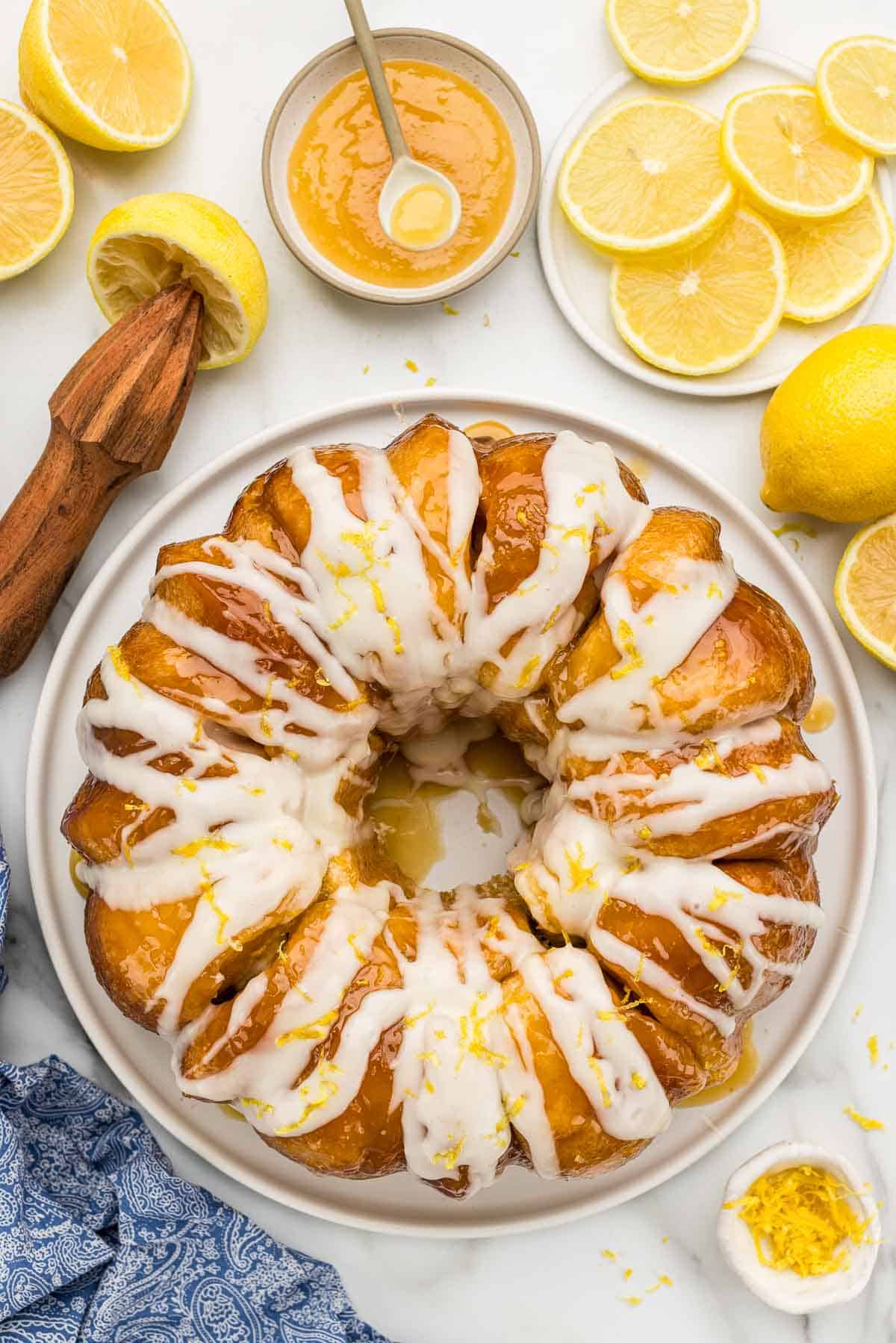Monkey bread on a cake stand surrounded by lemon zest, lemon slices, and a dish of lemon curd.