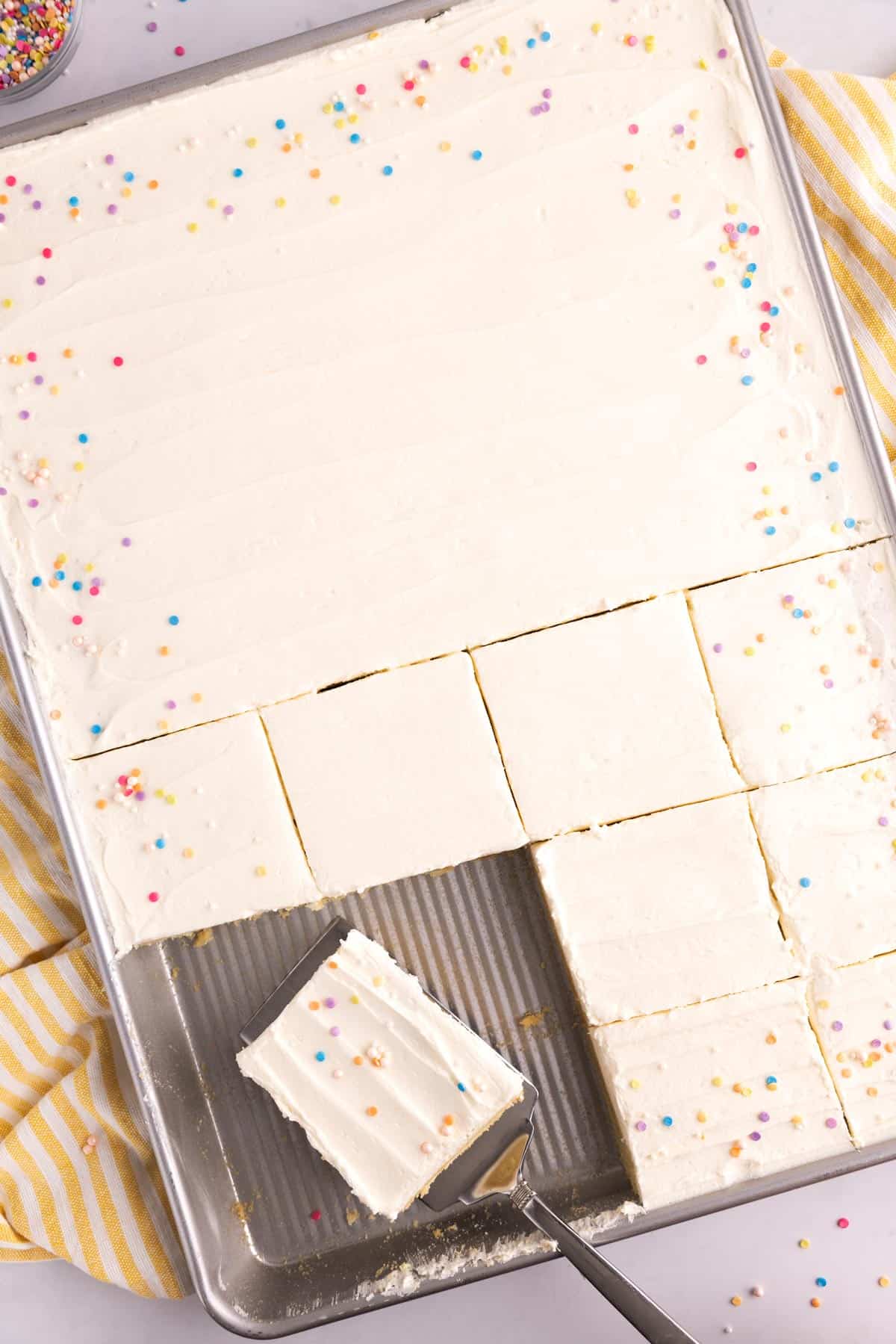 A square of sugar cookie being lifted out of a sheet pan on a serving spatula.