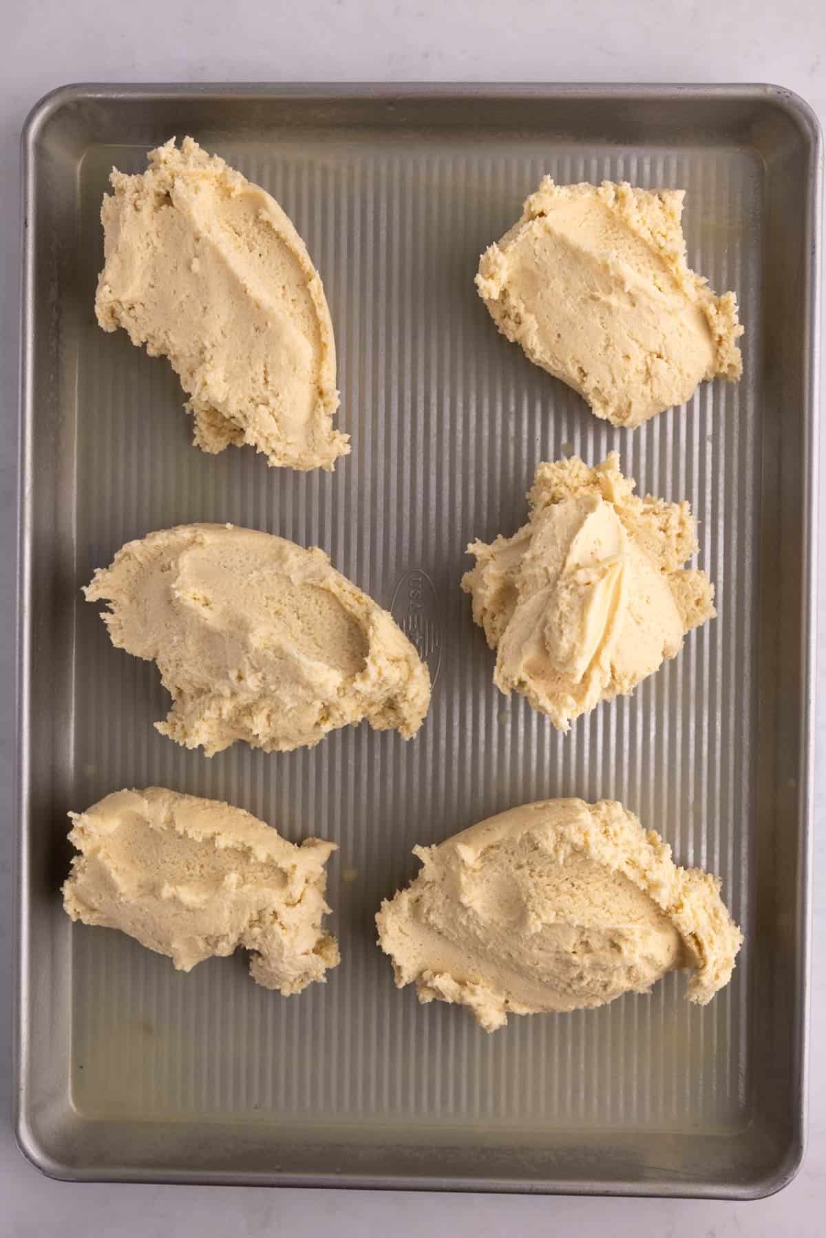 Blobs of cookie dough spread on a baking pan.