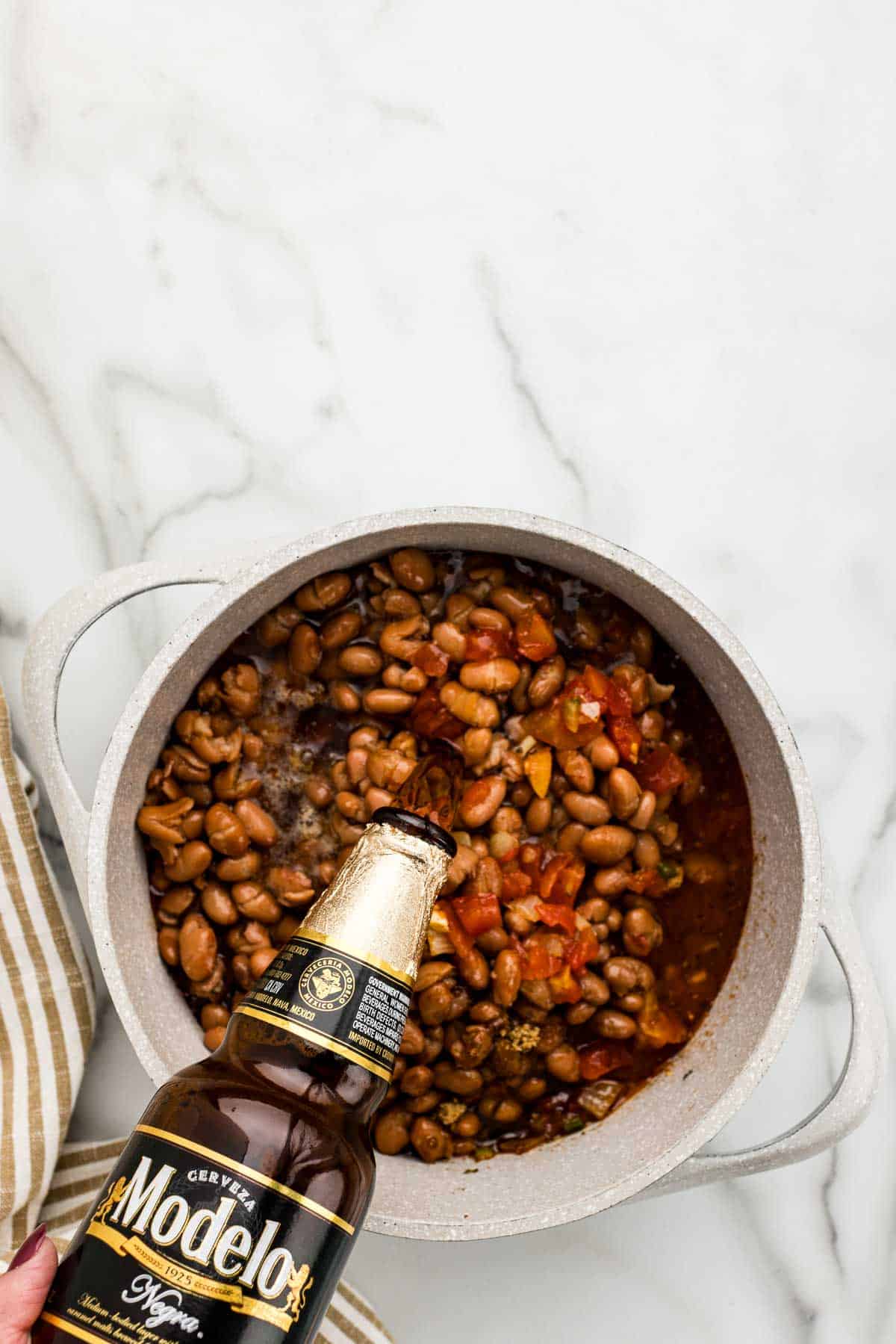 Beer getting poured into a pot of cooking beans.