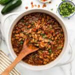 A wooden spoon taking a scoop out of a pot of borracho beans.