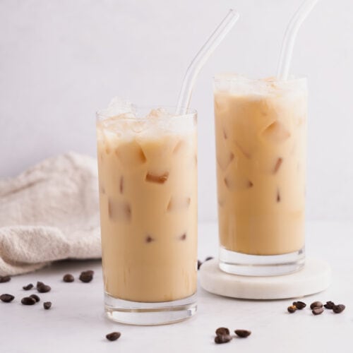 Two glass cups full of iced coffee beside each other with one on a coaster.