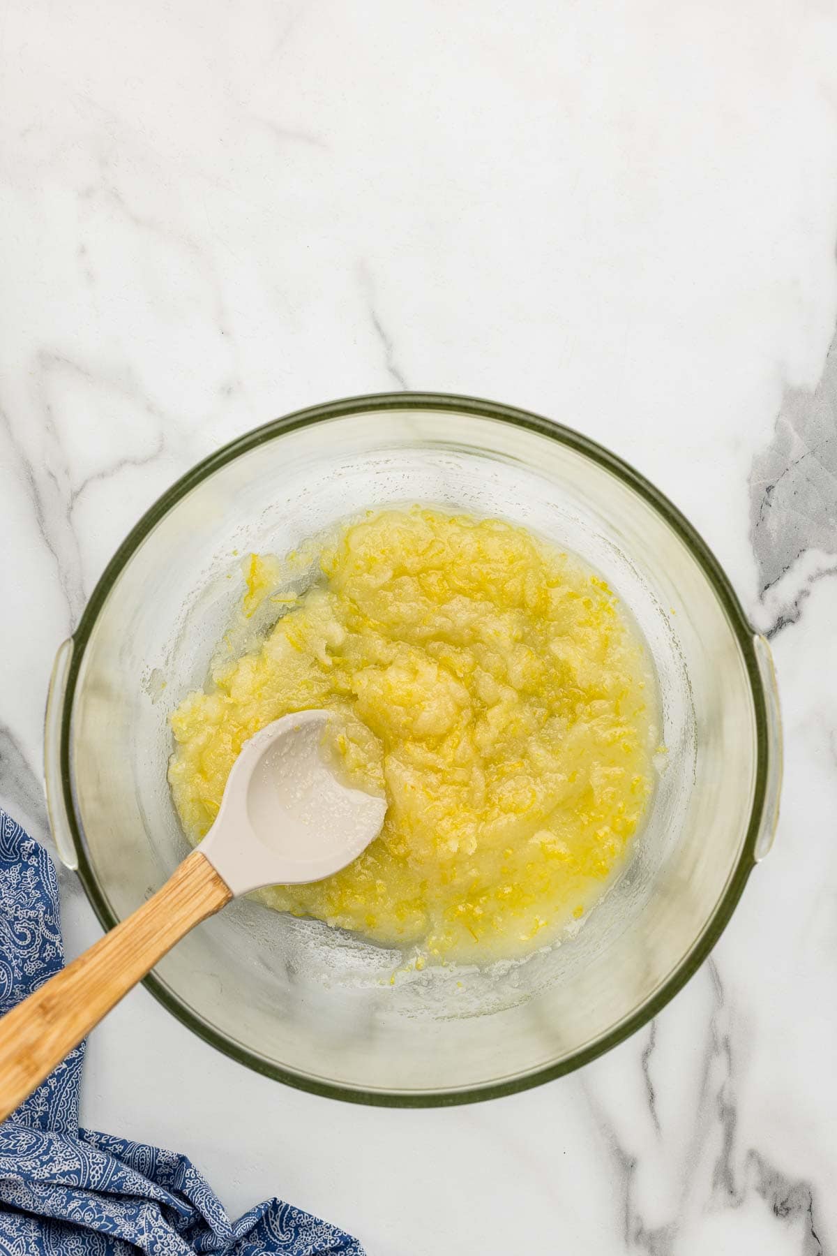 Lemon filling mixture in a glass bowl with a rubber-tipped wooden spoon.