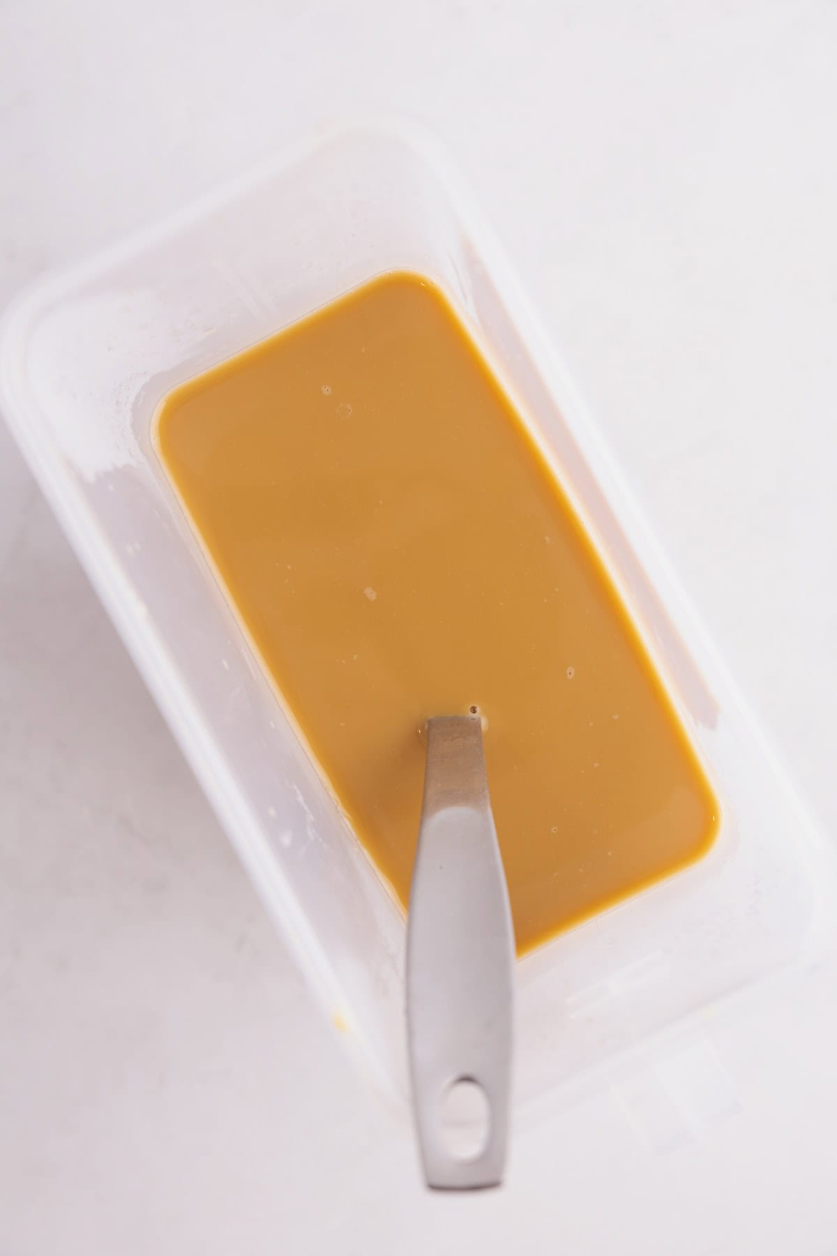 Condensed milk and coffee mixed in a plastic container with a mixing spoon.