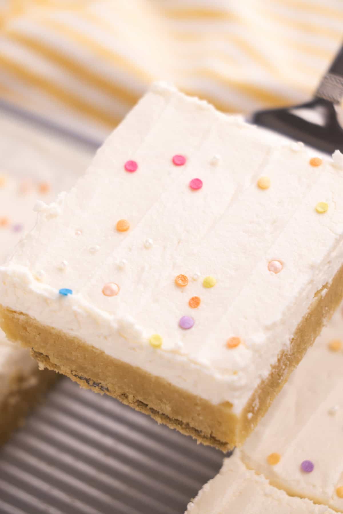 A spatula holding a sugar cookie square over a pan of cookie bars.