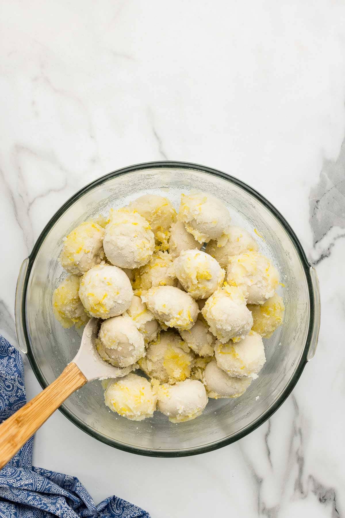 A bowl of dough balls rolled in lemon sugar with a wooden spoon.