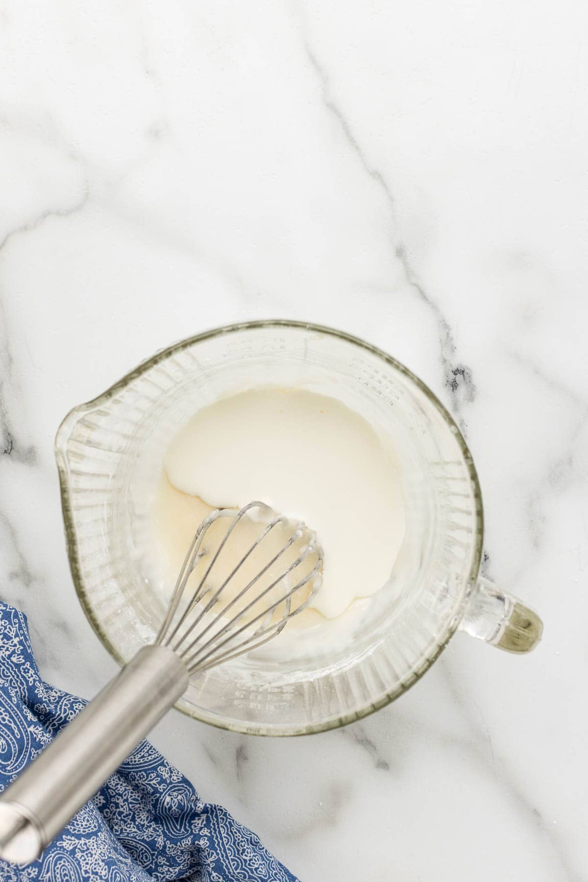A glass mixing bowl of monkey bread topping with a whisk.