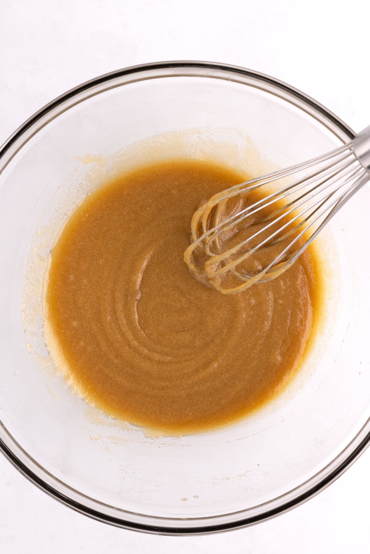 A whisk mixing carrot cake batter in a glass bowl.