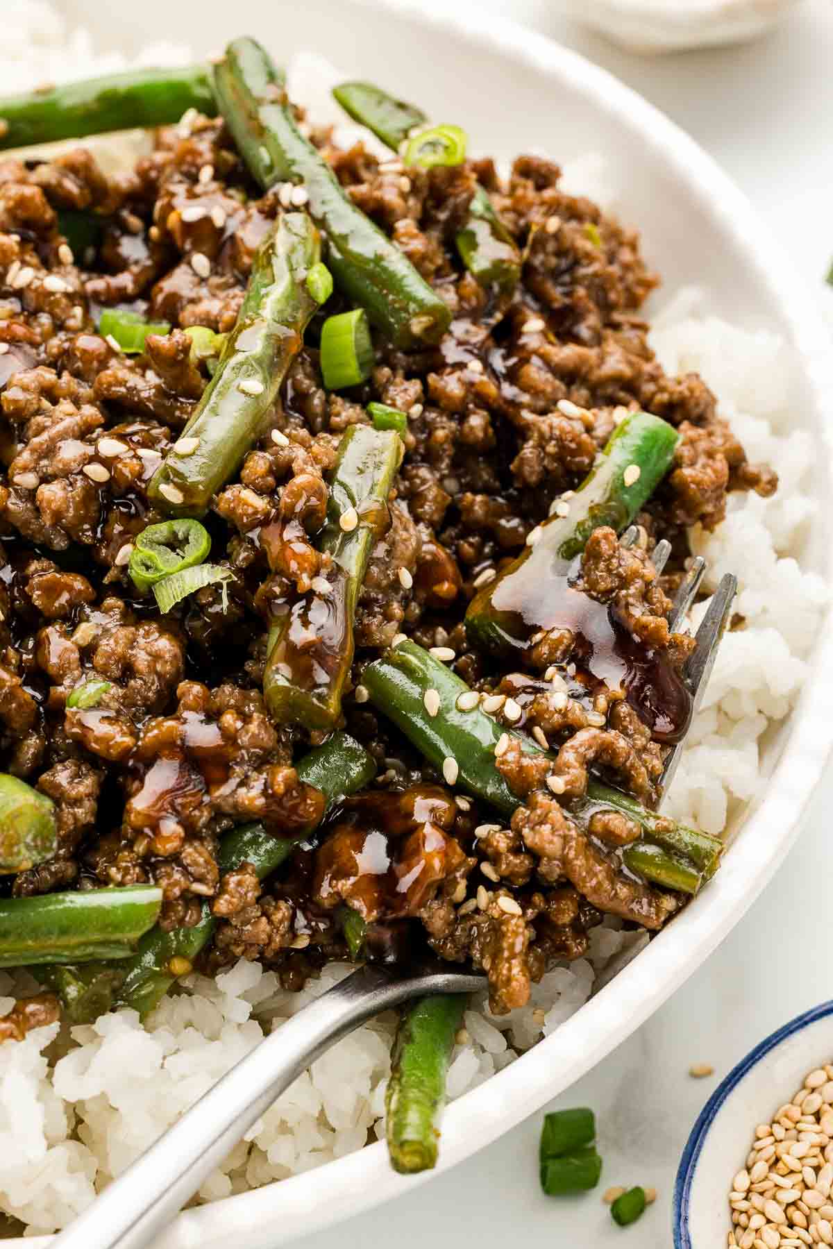 Closeup of sesame ground beef in a serving bowl with a fork.