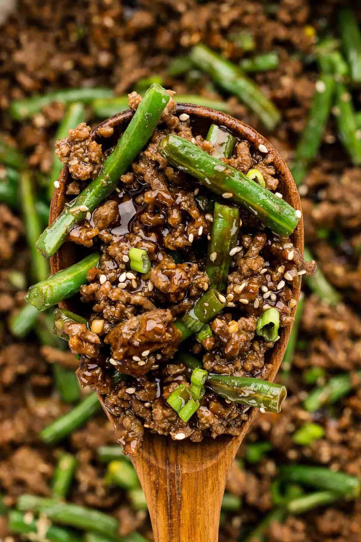 A scoop of ground beef and green beans on a wooden cooking spoon.
