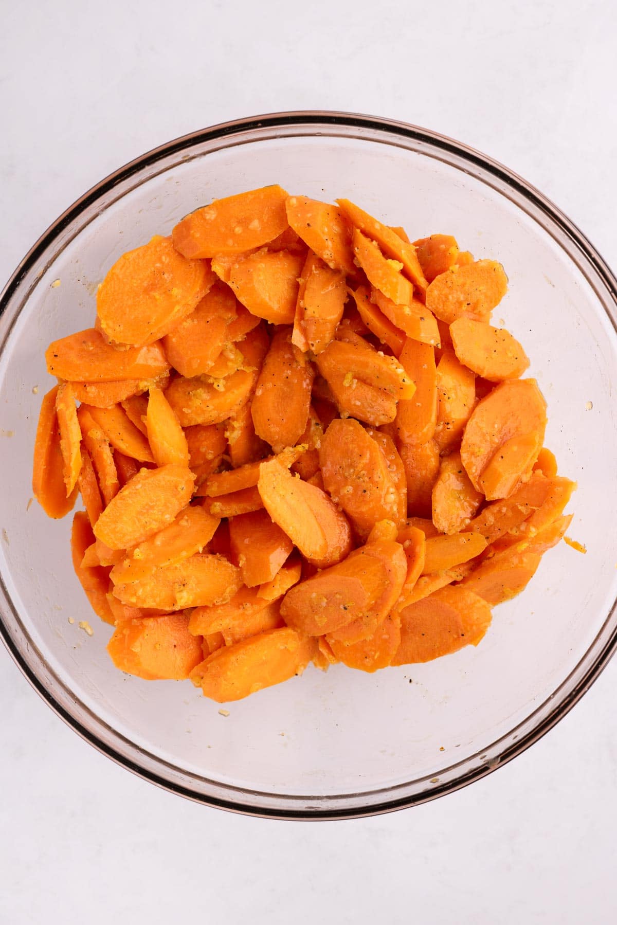 A glass mixing bowl with sliced carrots covered in honey glaze.
