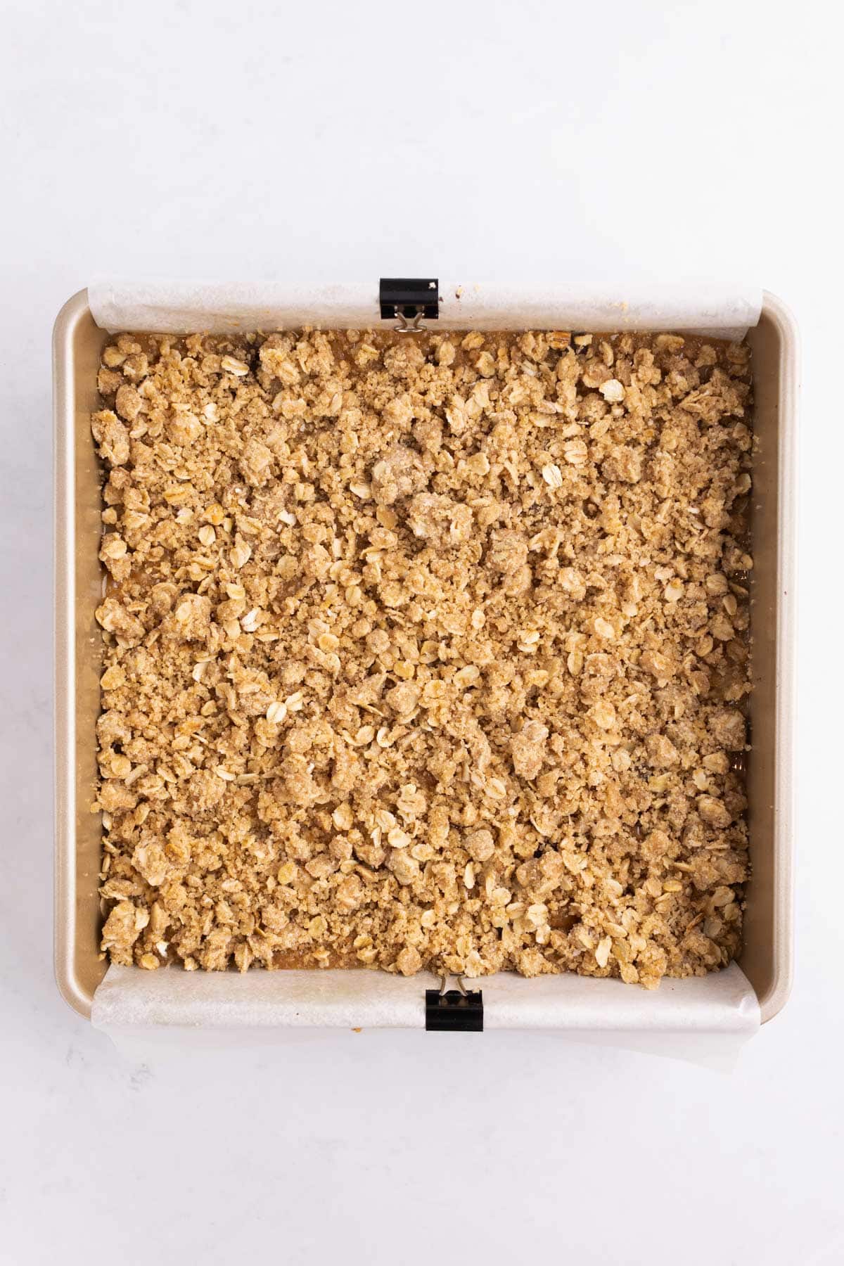 Oats sprinkled on top of caramel filling in a square baking pan.