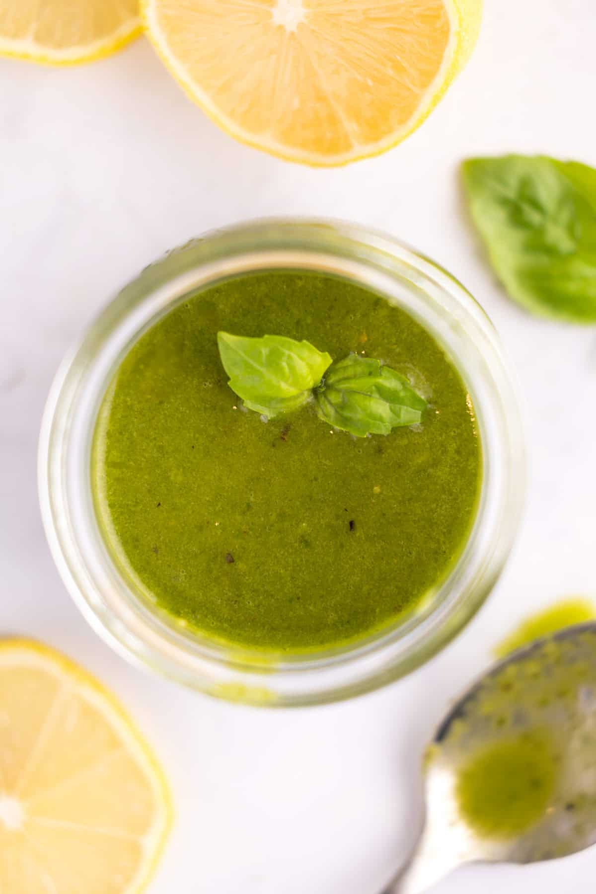 Overhead of a glass jar of lemon basil vinaigrette with a basil leaf on top.