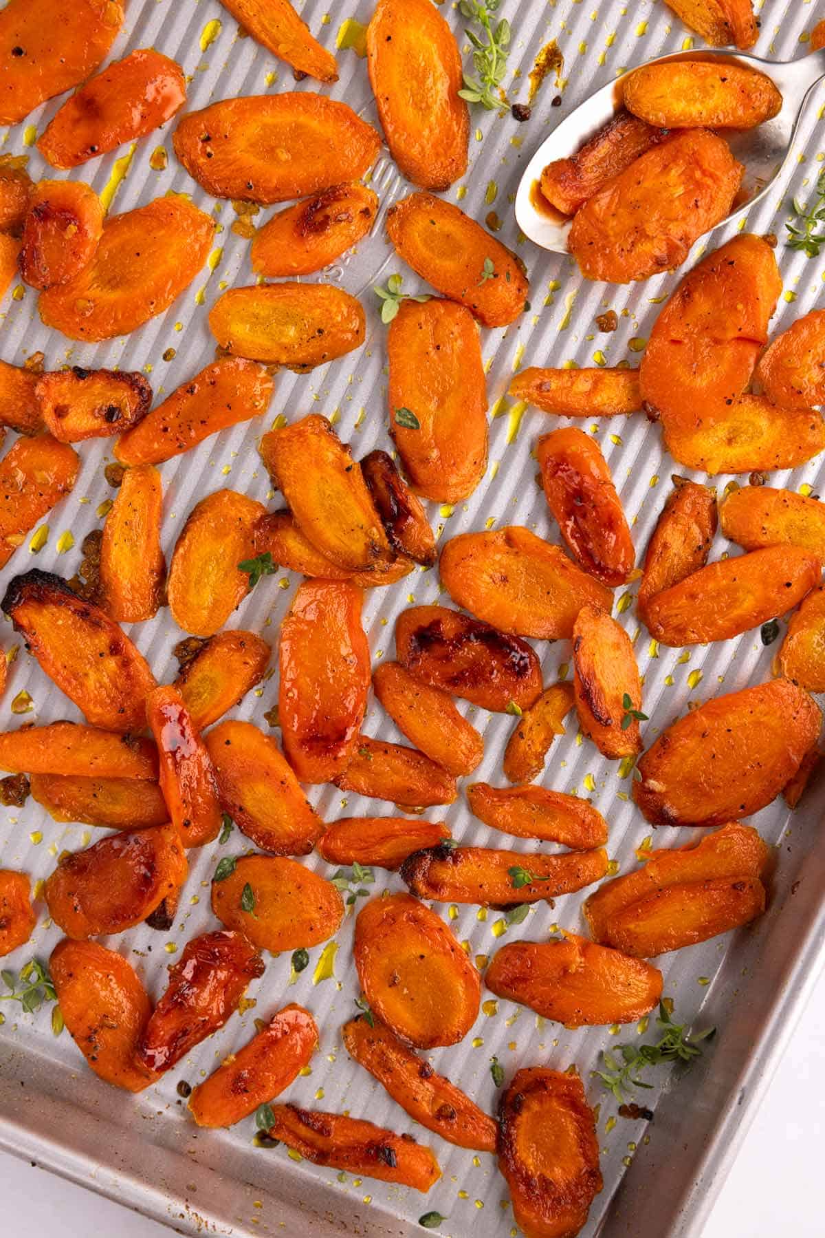 A pan of roasted honey carrots with a spoon.