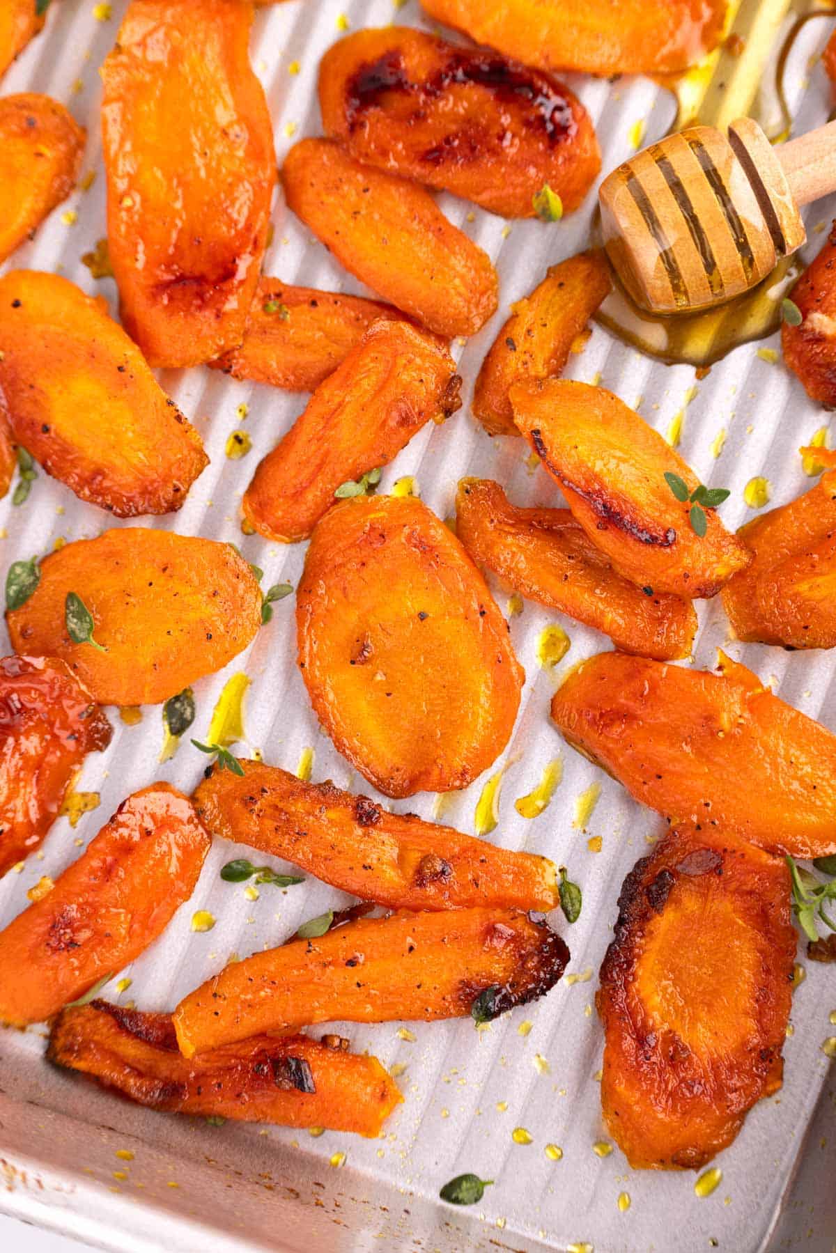 A pan of roasted carrots with a honey stick full of honey resting at the top.