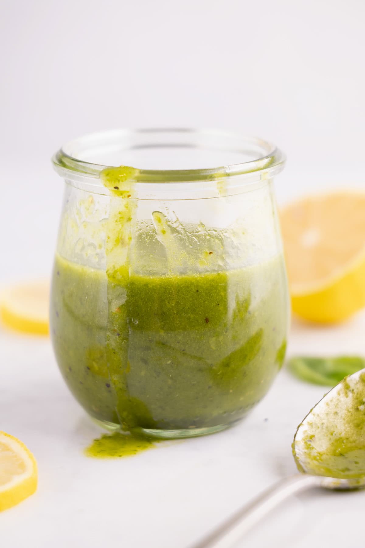 Lemon basil dressing in a glass container with a spoon beside it.