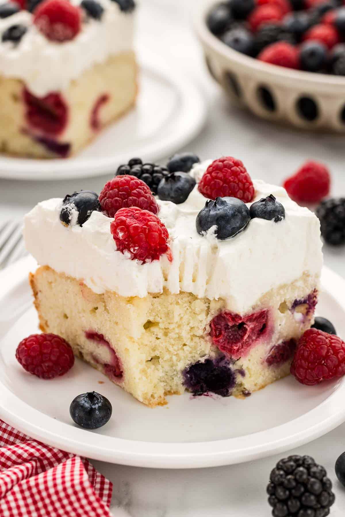 A bite taken out of a square of mixed berry cake on a small serving plate.
