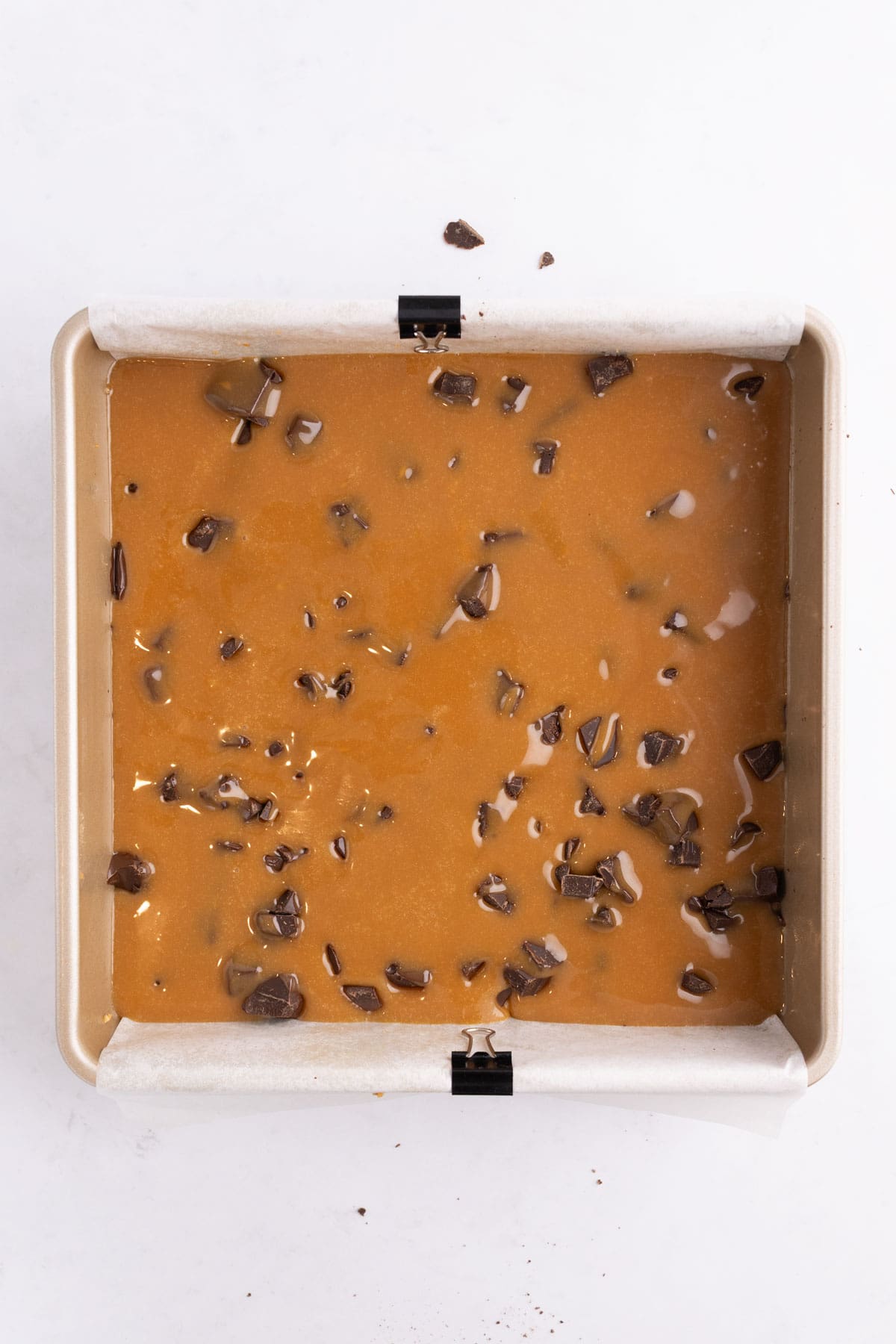 Caramel filling settled into a baking pan with chocolate chunks.