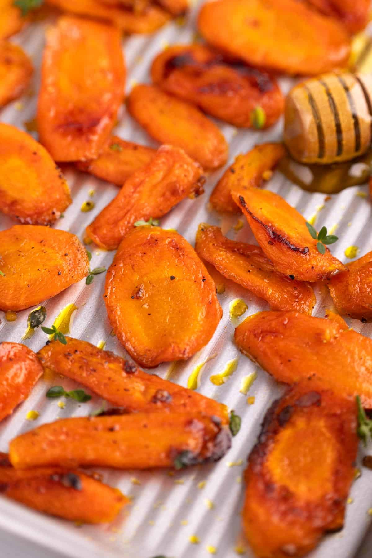Slices of roasted carrots with a honey stick beside them.