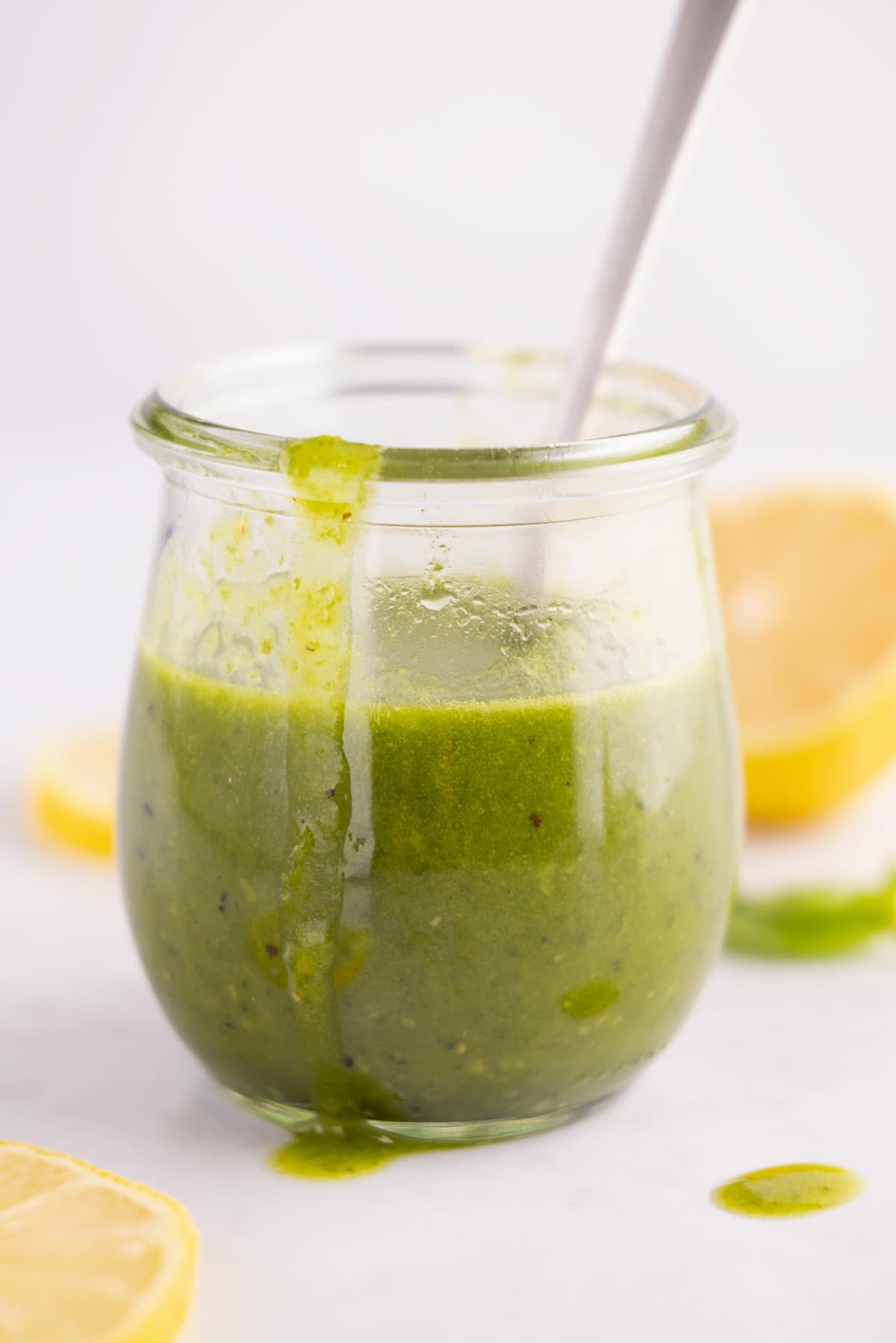 A spoon sticking out the top of a jar of lemon basil vinaigrette.