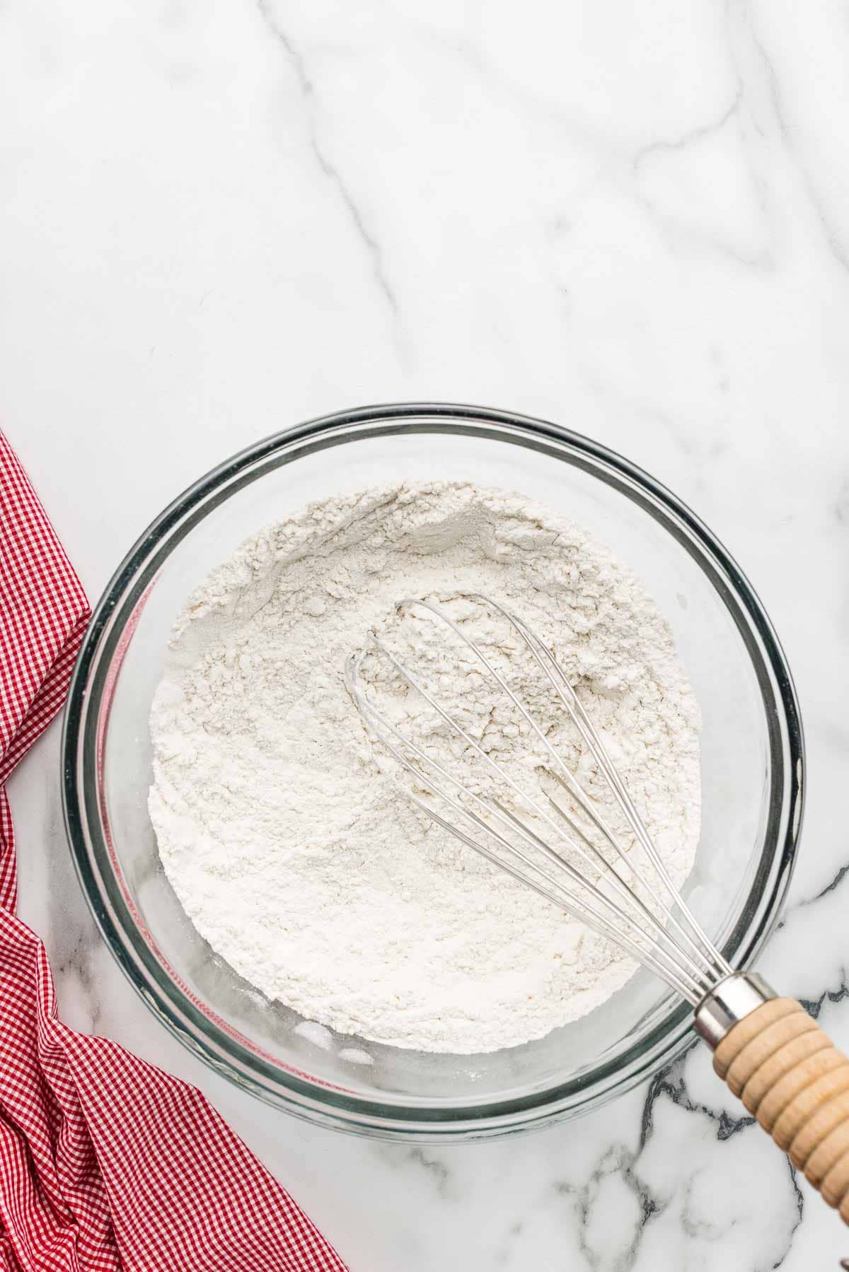 Dry ingredients in a glass bowl with a whisk.