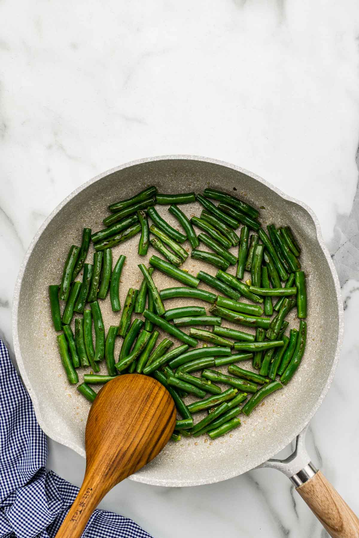 A skillet of green beans with a wooden spoon.