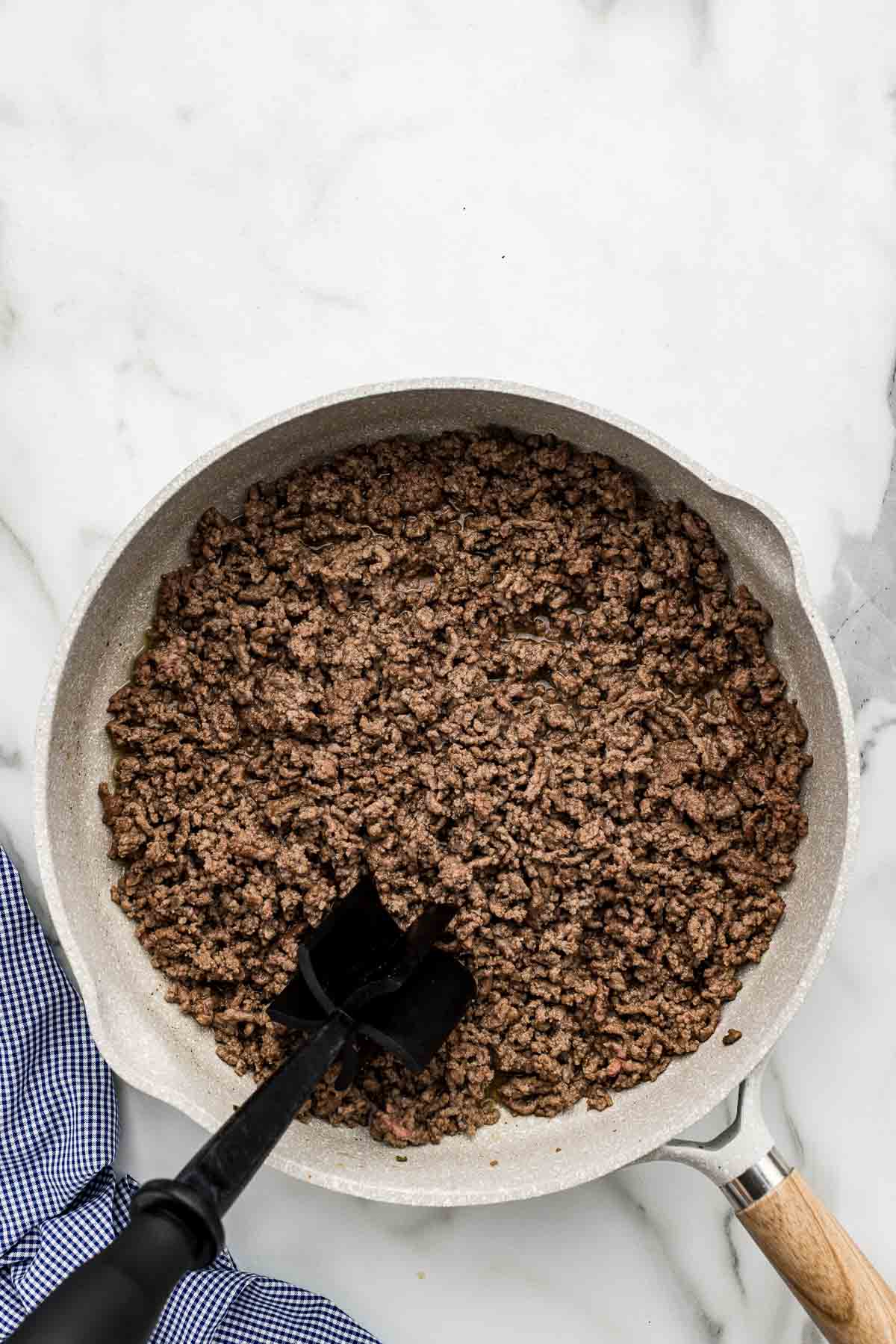 Beef being ground with a tool in a large pan.