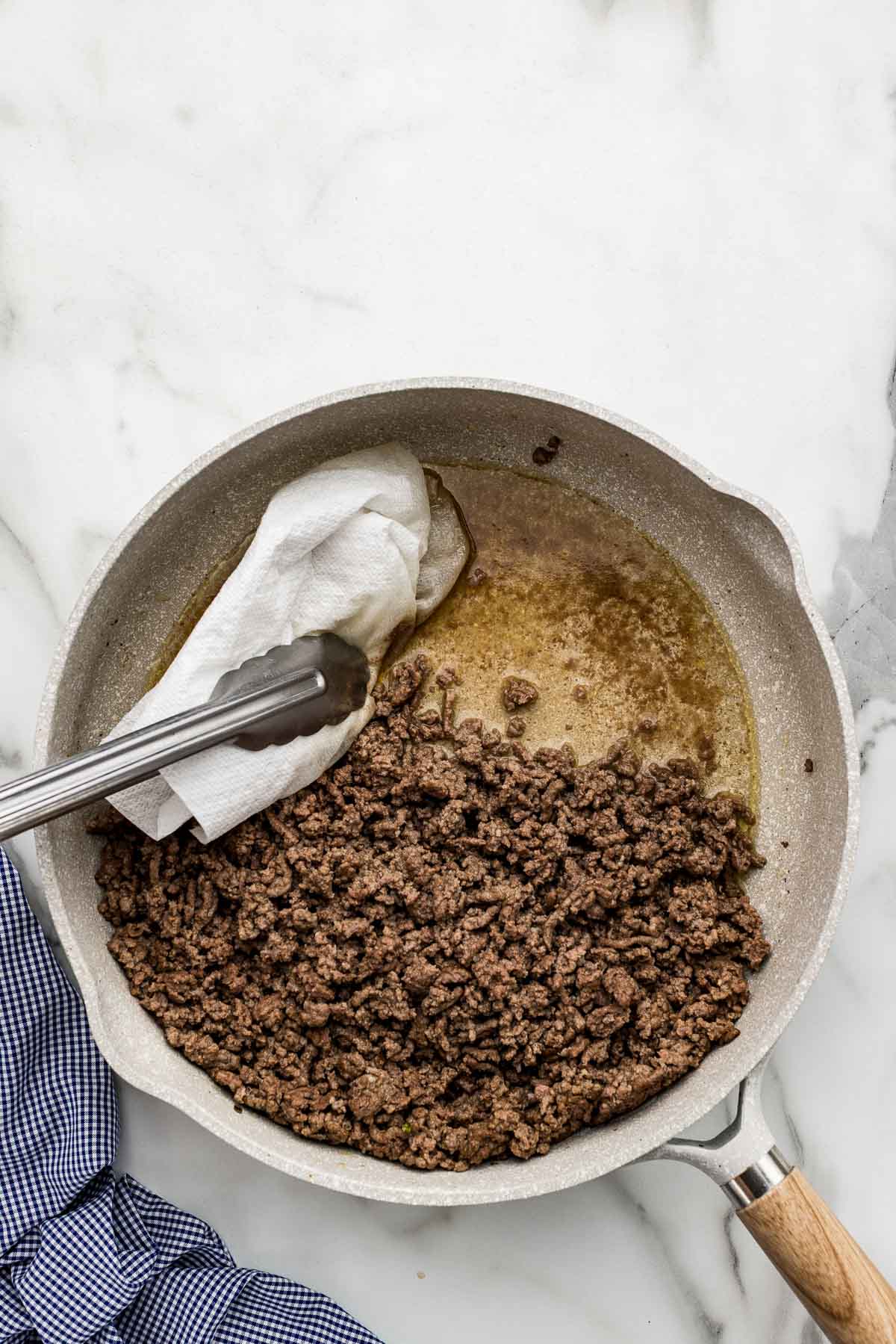 A paper towel soaking up the beef juices between a pair of tongs.