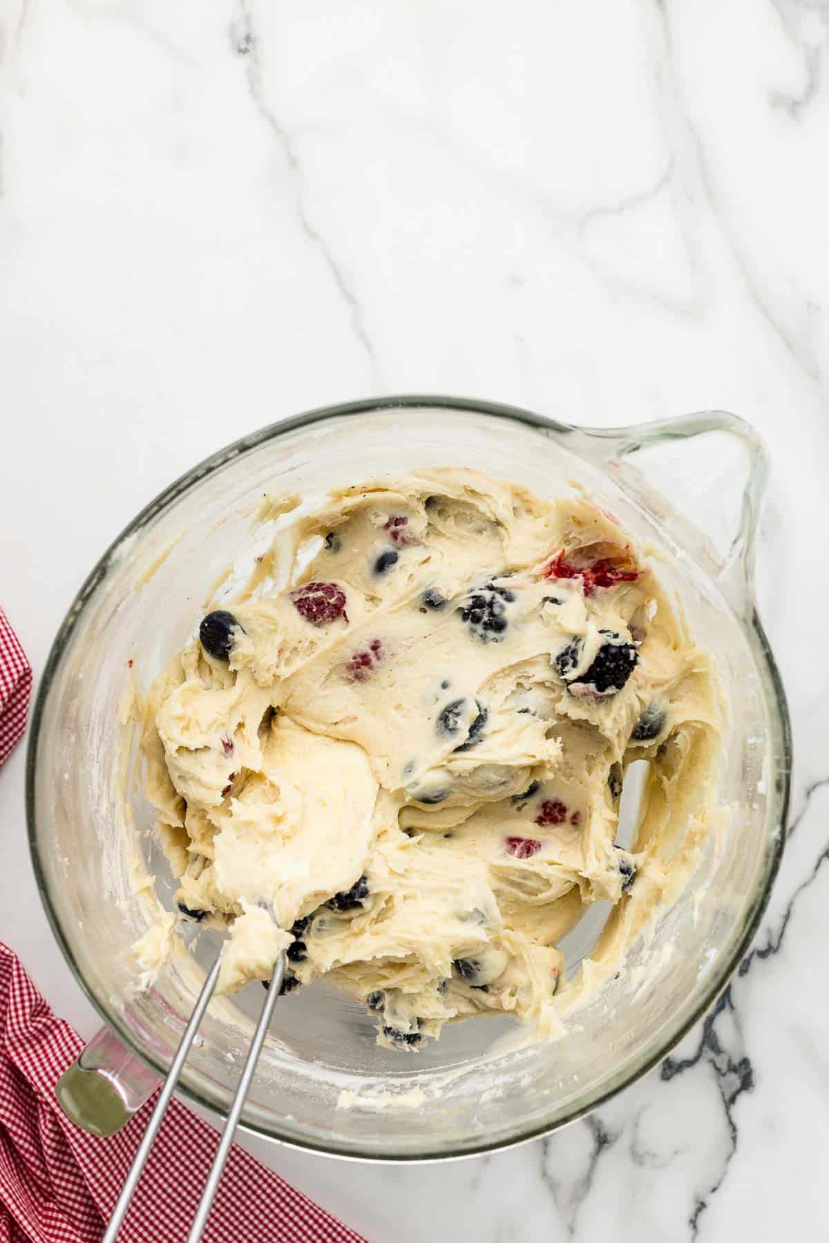 A rubber spatula folding berries into cake batter.