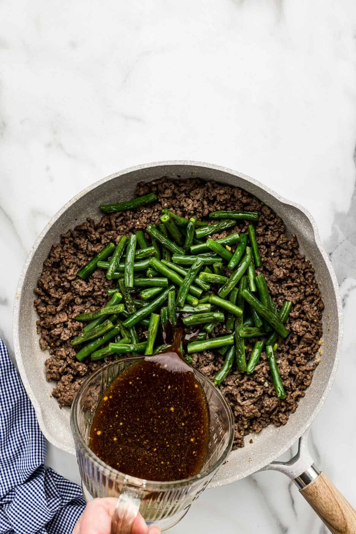 Green beans and sauce added to a large pan of beef.