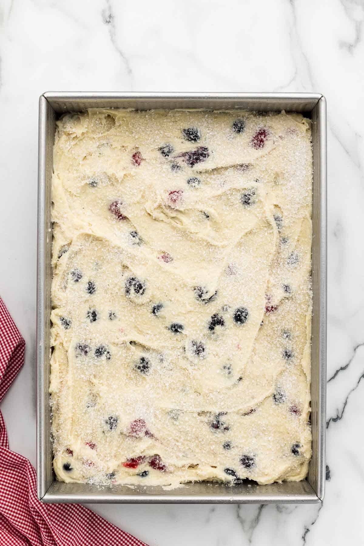 Berries and cake batter in a baking pan topped with sugar.