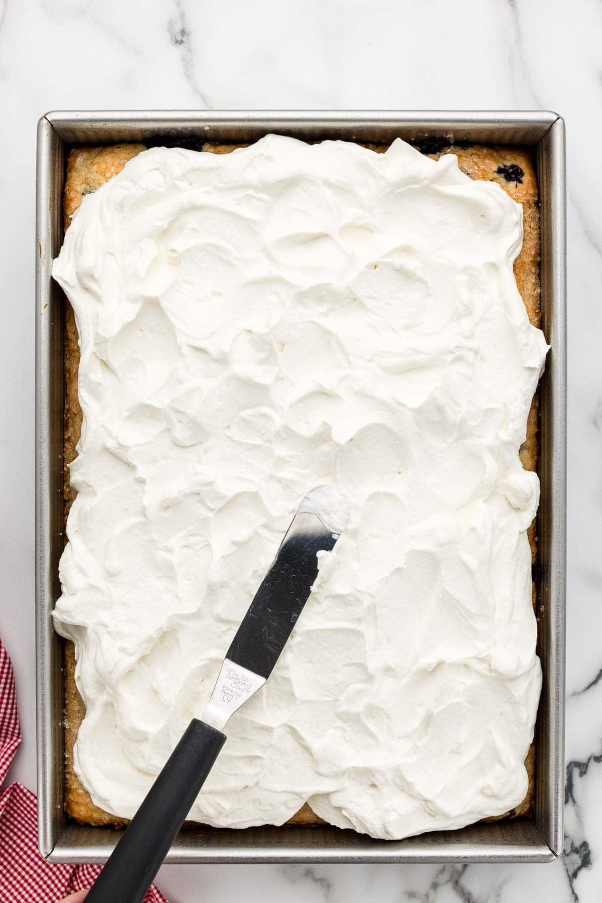 Cream cheese frosting being spread with an offset spatula on a berry cake.