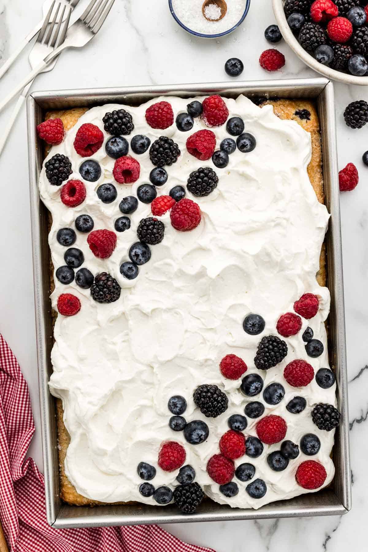Mixed berry cake in a 9x13 baking pan with topped with frosting and fruit.