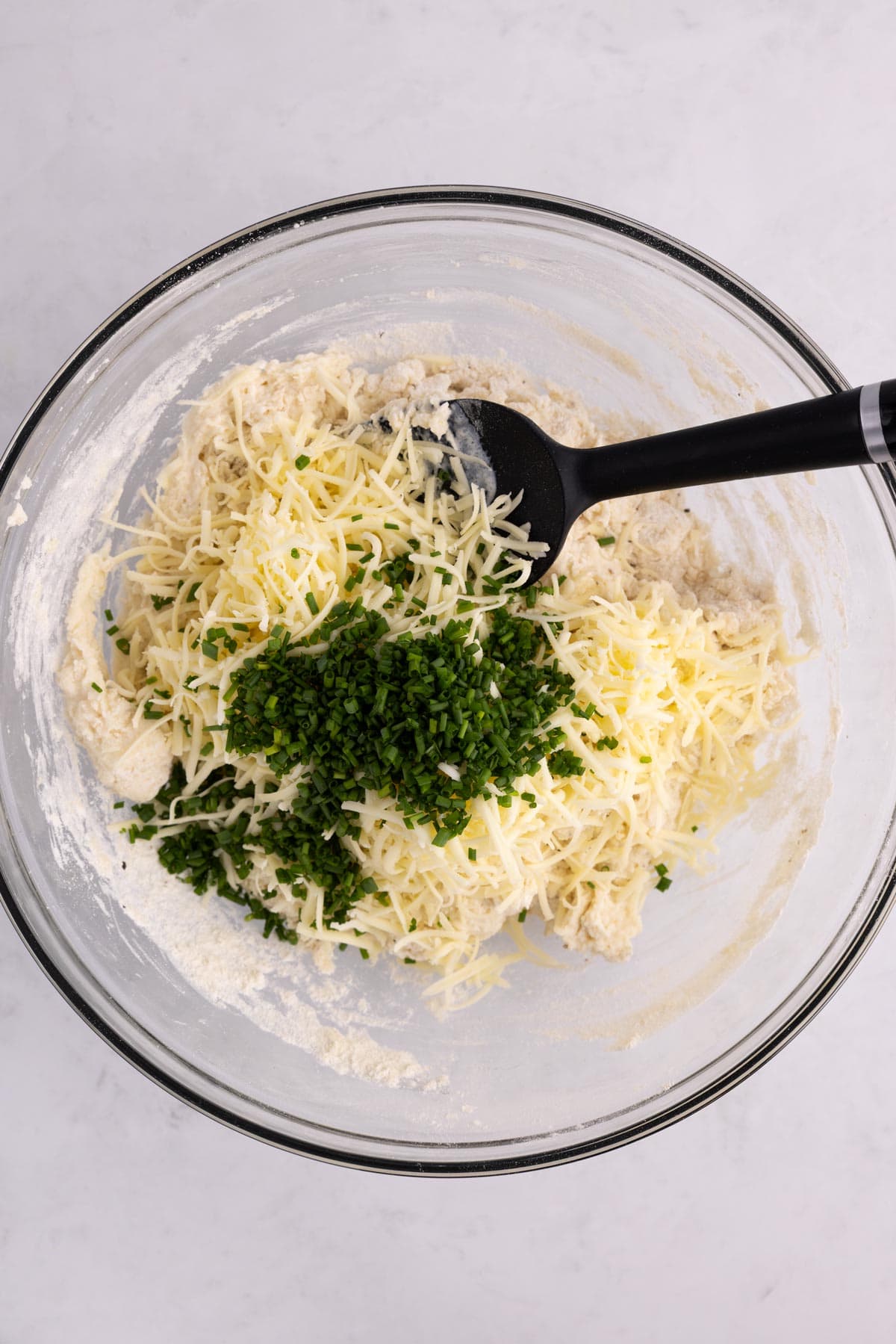 Cheese and herbs added to a bowl of biscuit dough.