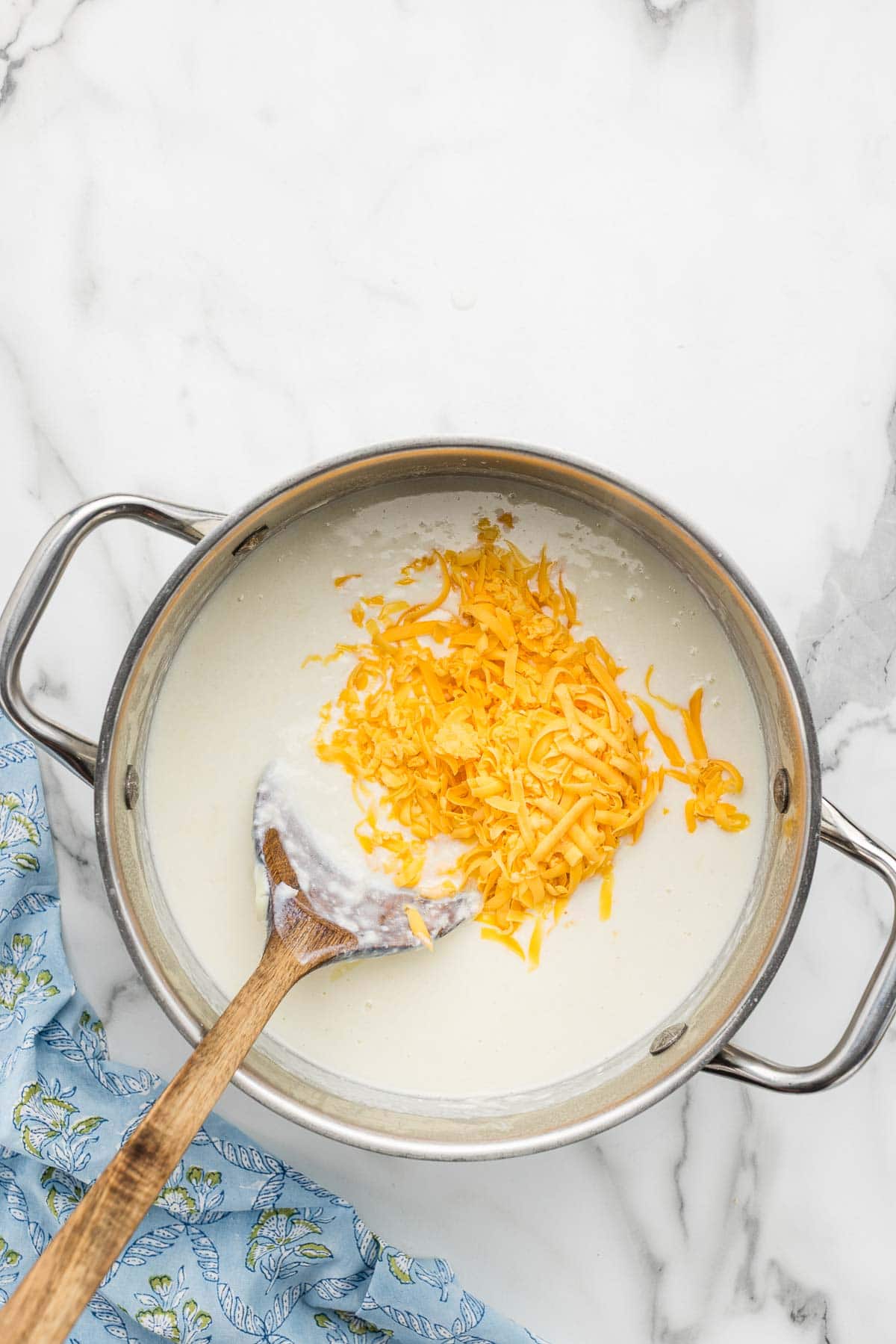Cheese added to a pot of creamy sauce with a wooden spoon.